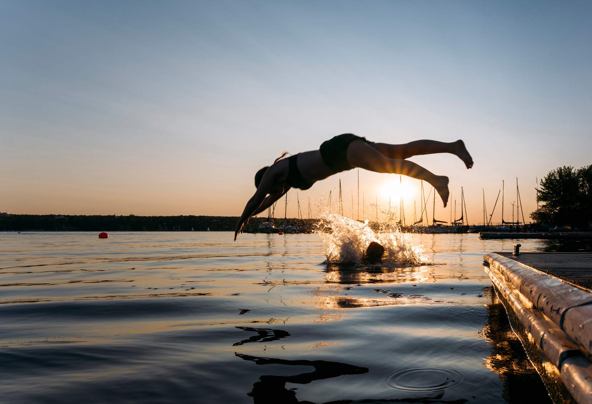 A person in a diving position above a lake with a water splash nearby.