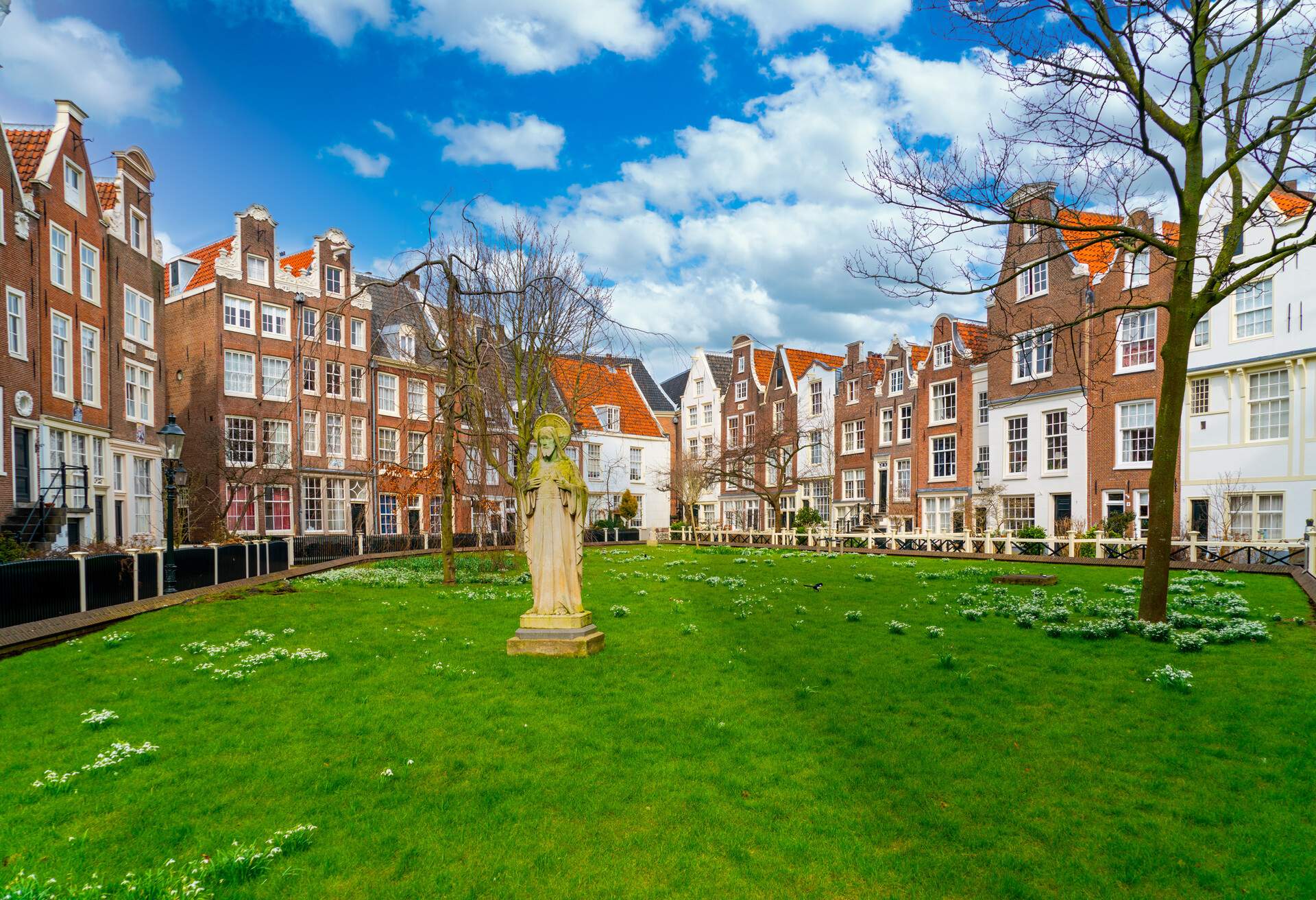 A park in Amsterdam surrounded by iconic narrow buildings and a statue in the middle on the grass