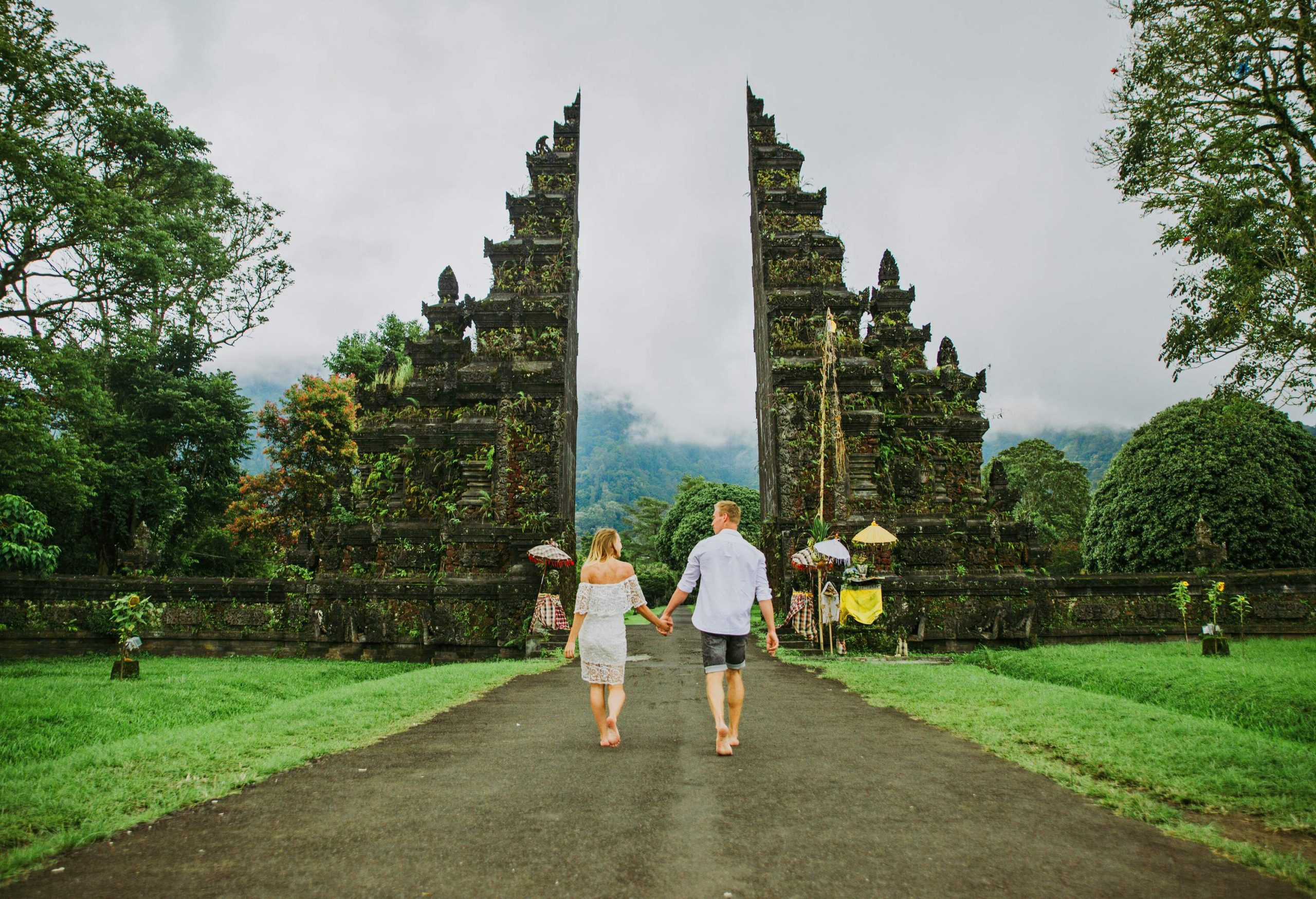 Couples walk hand in hand into the Handara Gate, a classic Javanese-Bali split gate surrounded by lush vegetation.