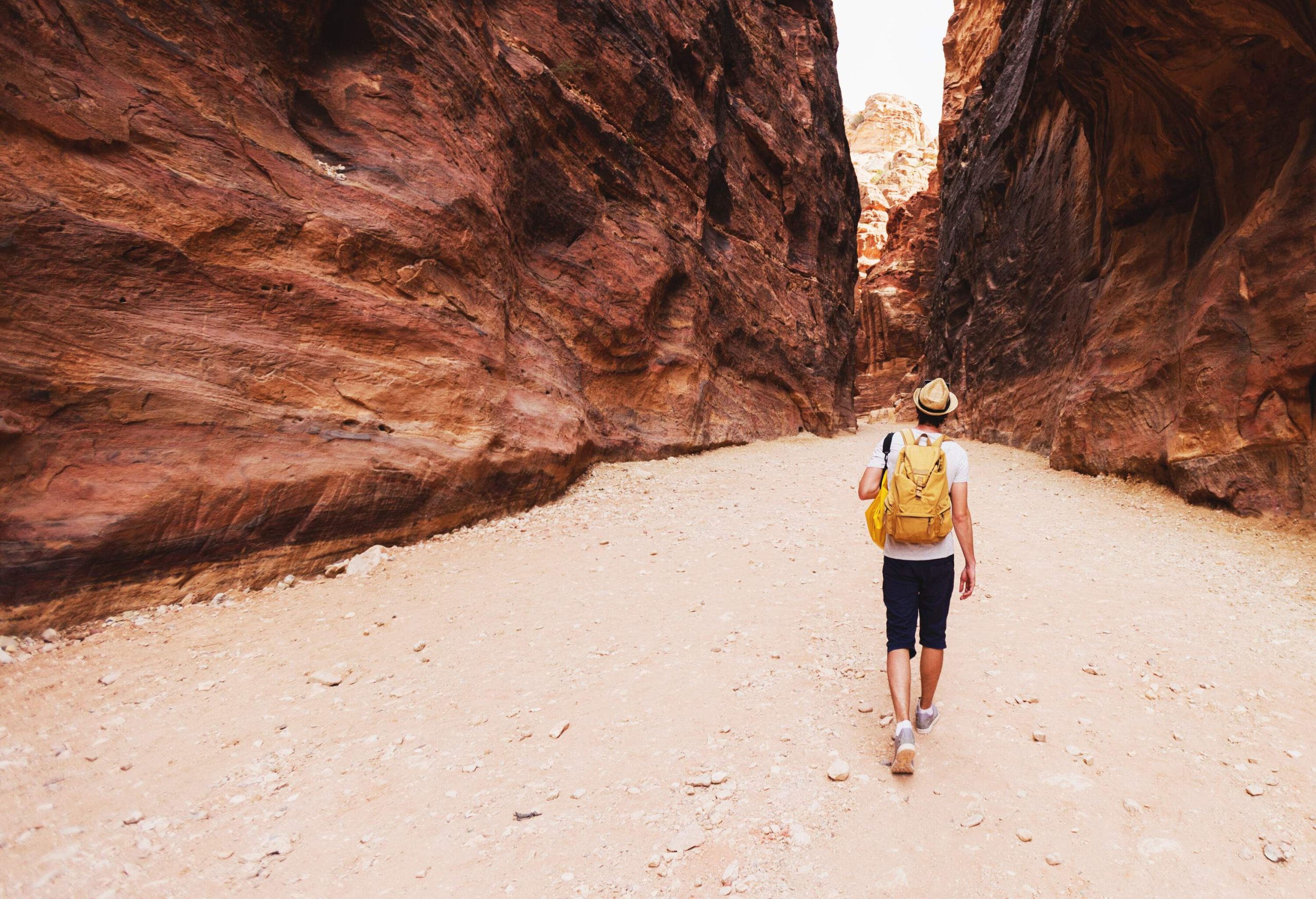 A hiker with a hat and a backpack makes his way to the narrow trail that runs between the canyons.