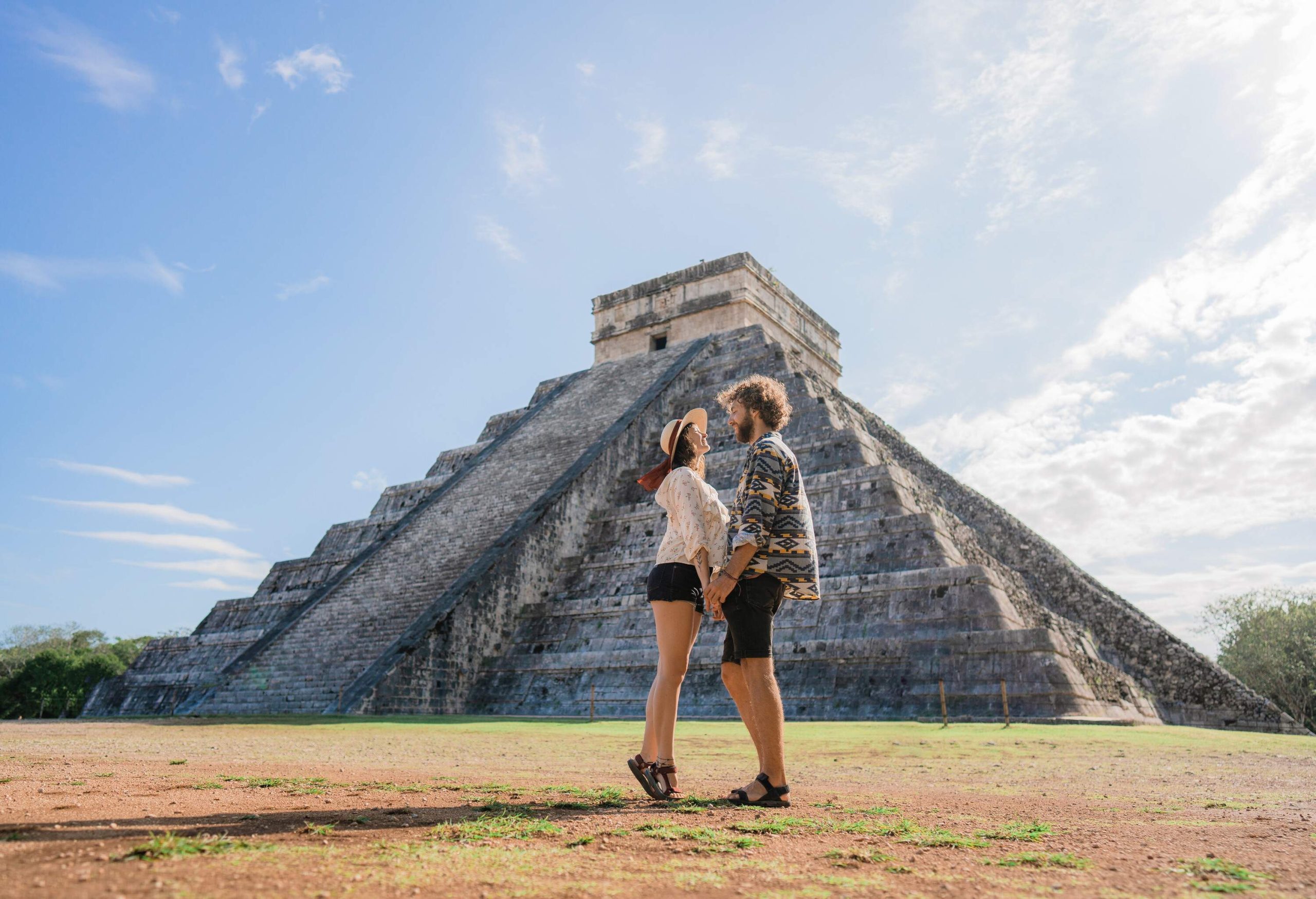 A couple holds hands facing each other in front of a Mesoamerican step pyramid.
