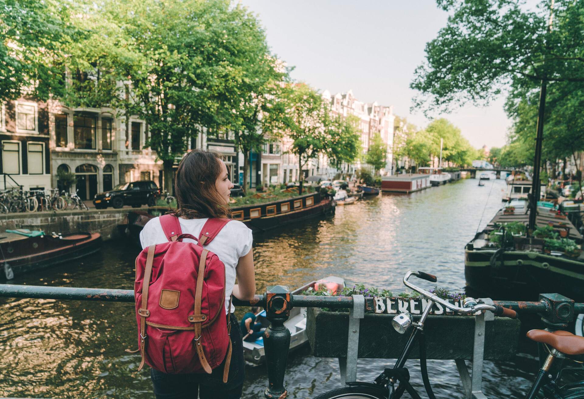 A young woman standing on the side of a bridge over a canal with boats.