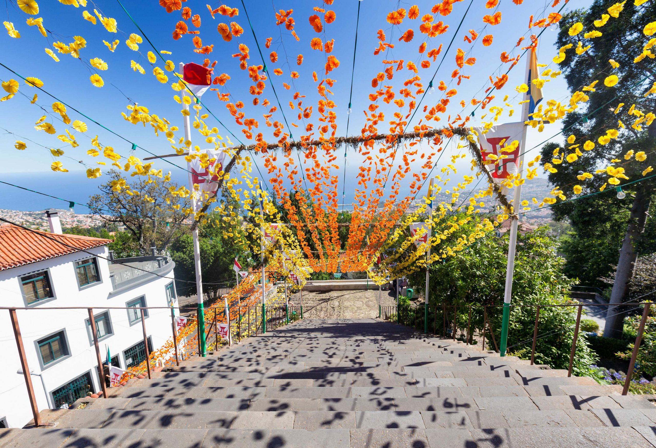 A descending stairway decorated with hanging yellow and orange paper flowers on a sunny day.