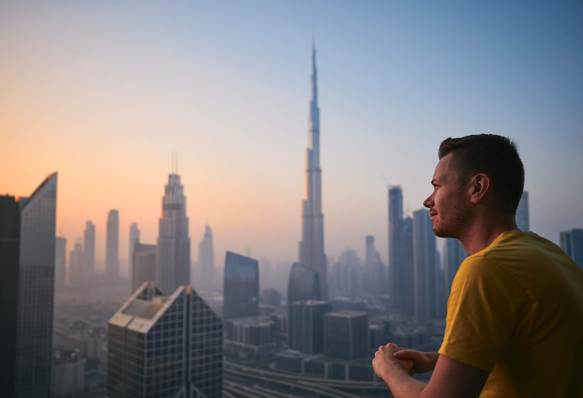 A man on a terrace looks at a city skyline with skyscrapers on a foggy morning.