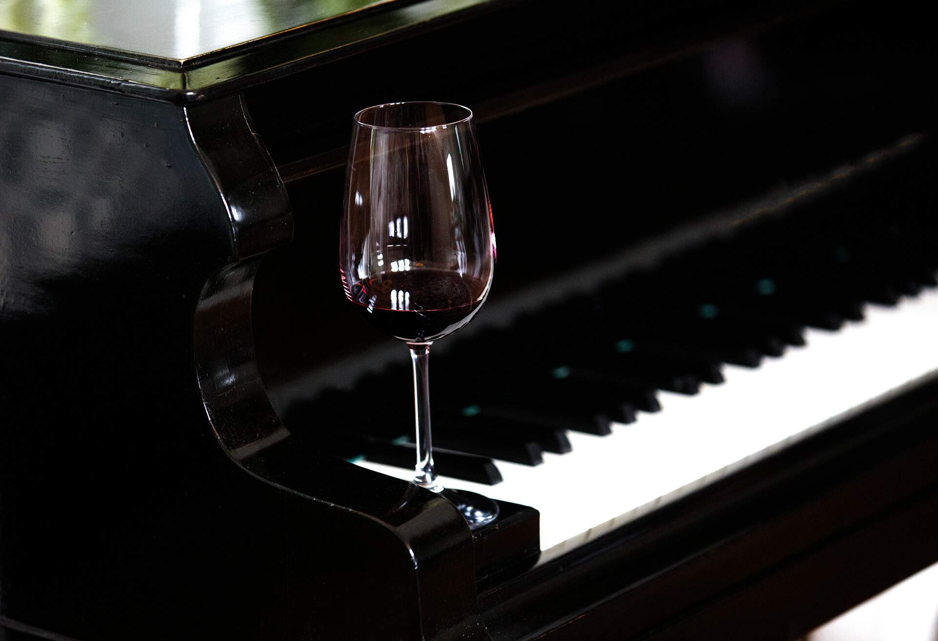 A glass of wine delicately placed at the edge of a piano.