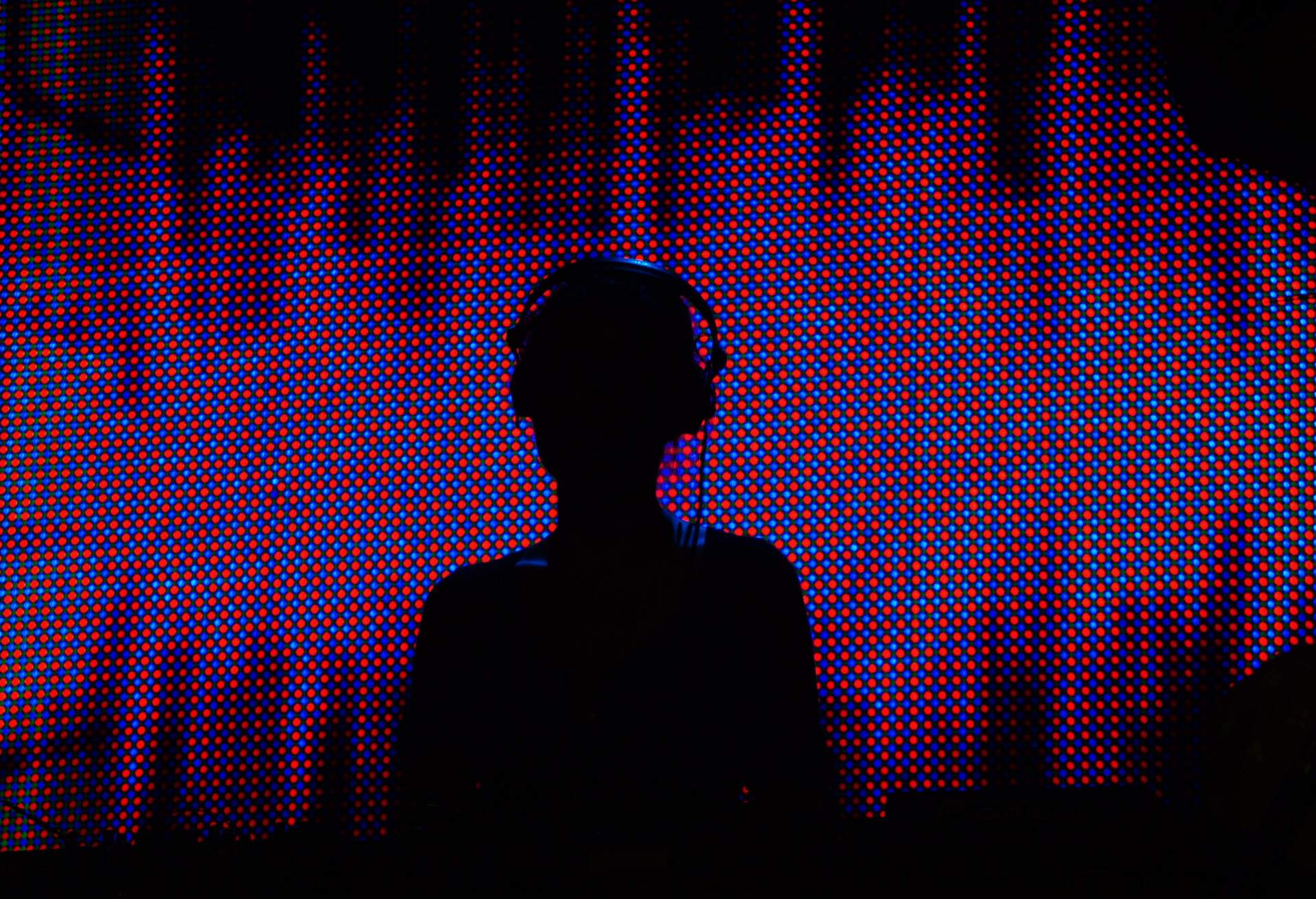 A DJ's silhouette against a neon background in a nightclub.