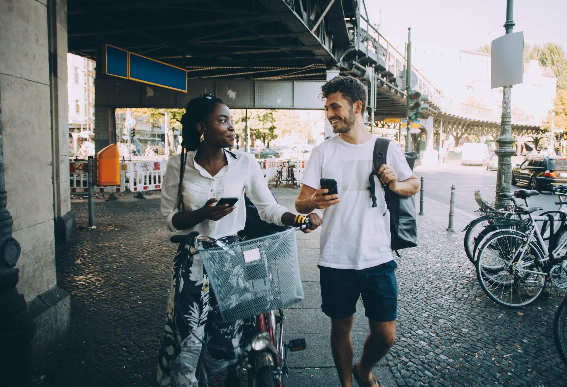 A man and a woman with a bike smiling at each other as they walk along a sidewalk.