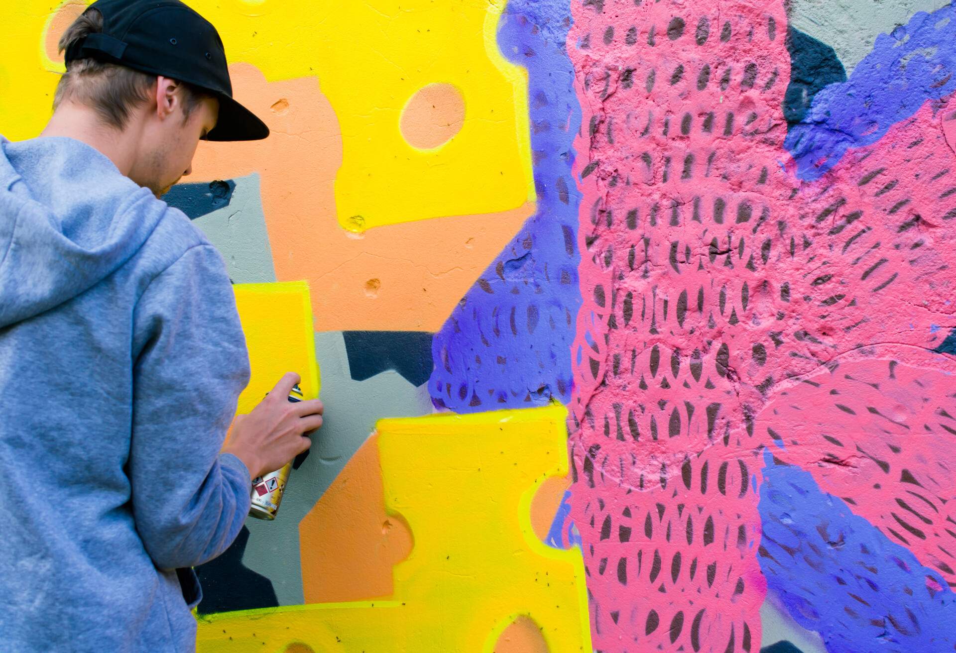 A man spraying paint on a brightly coloured wall graffiti.