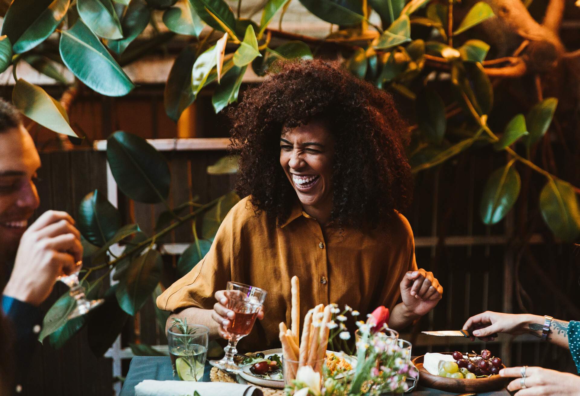 A happy woman with beautiful curly hair enjoys meals and wine with her colleagues.