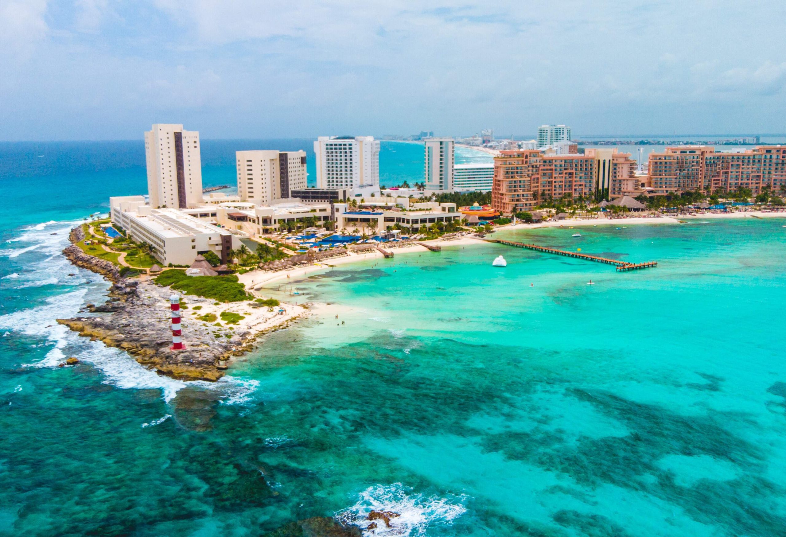 A coastline's edge with a lighthouse and clusters of tall hotels overlooking a turquoise beach.