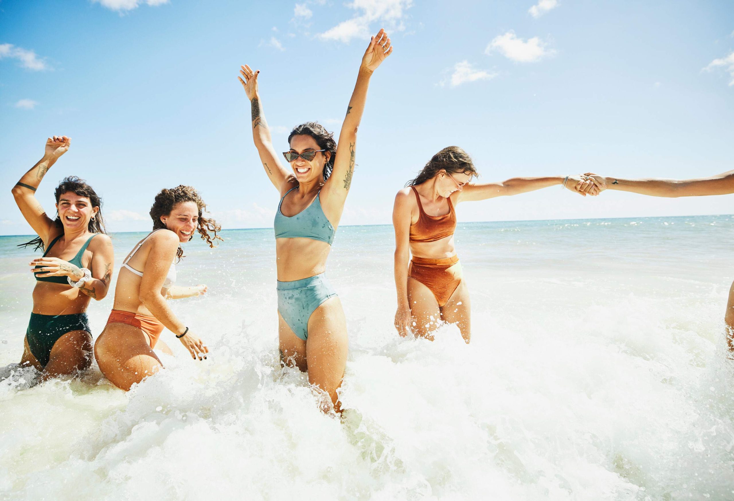 A group of friends, donning two-piece swimsuits, joyfully splash and playfully get smashed by crashing waves.