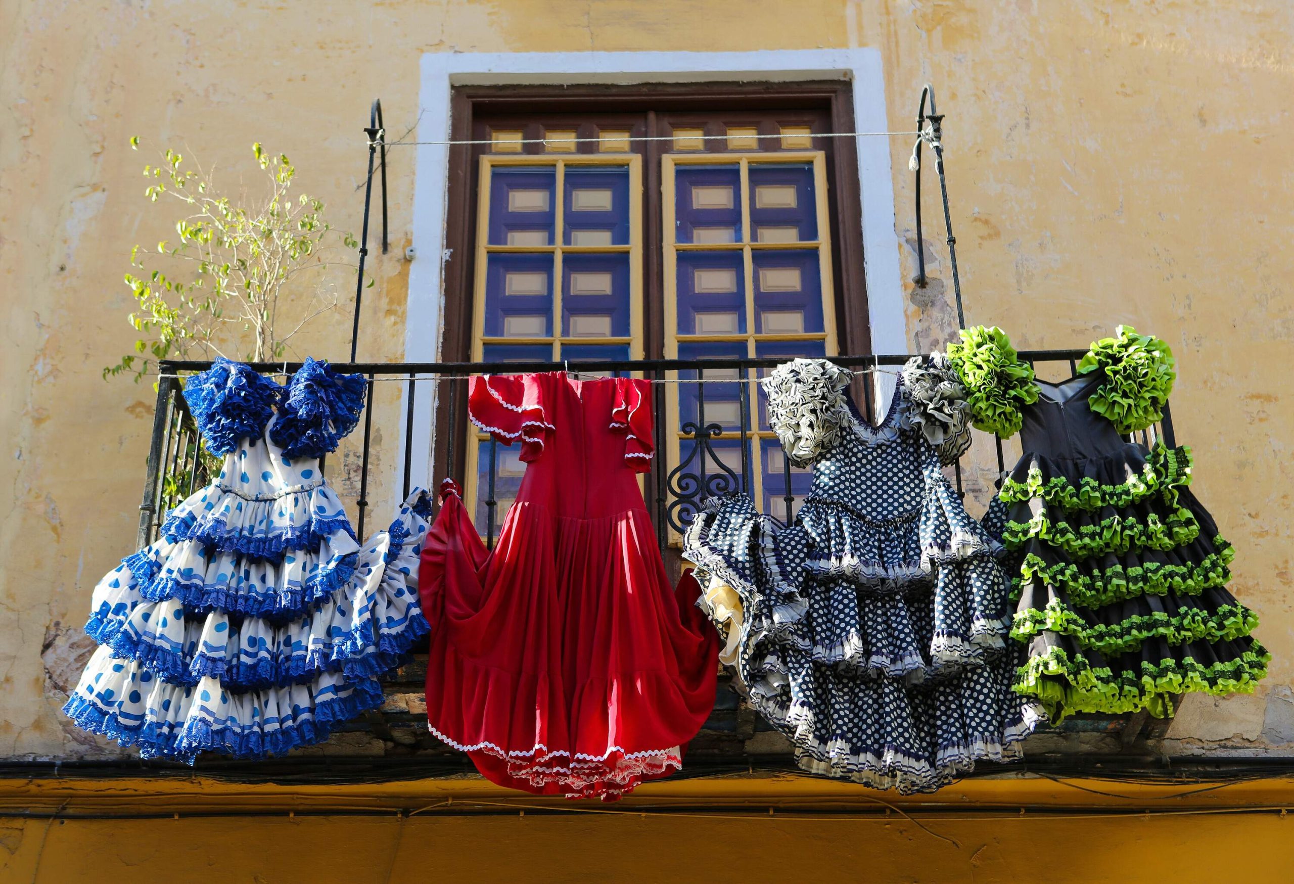 Four unique and colourful flamenco outfits hanging from a balcony railing.