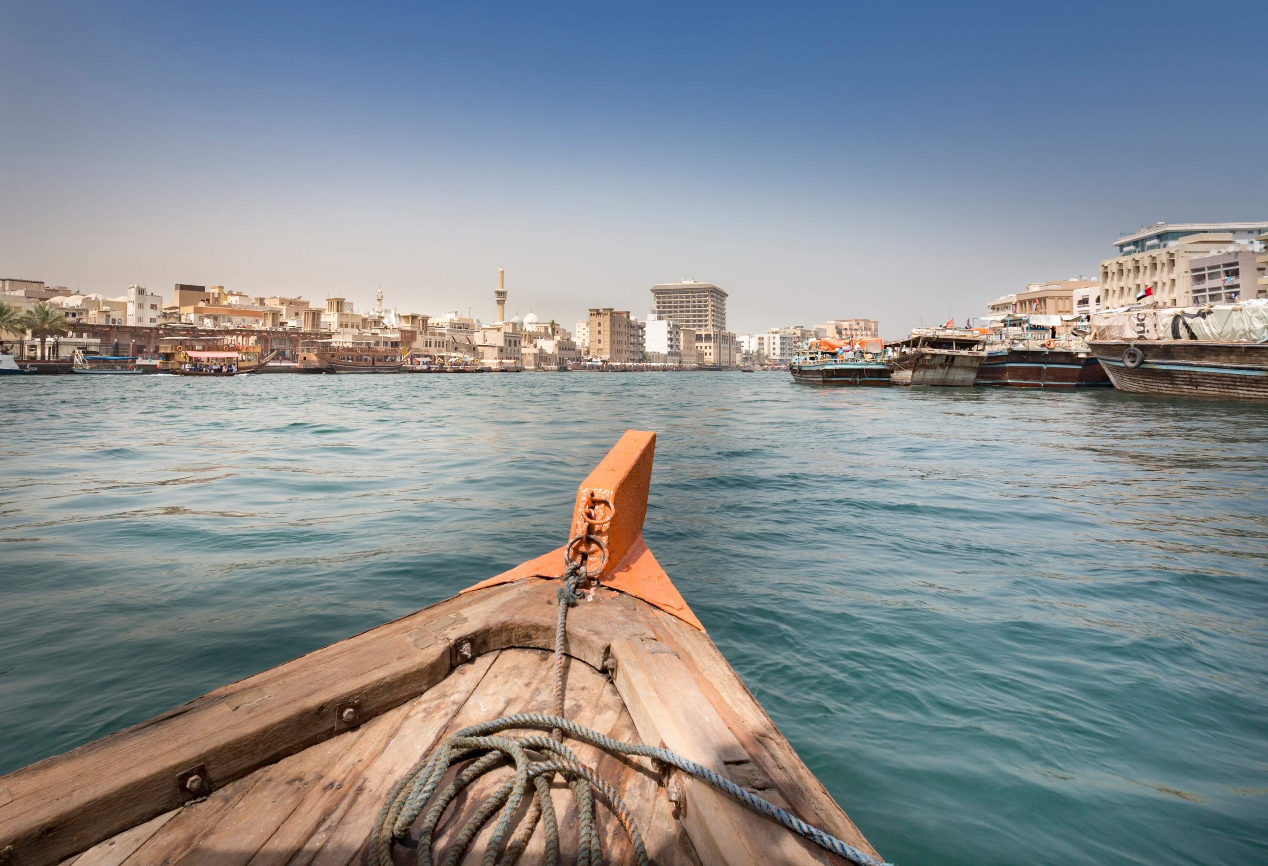 A wooden boat travelling across the water, with buildings along the coast.