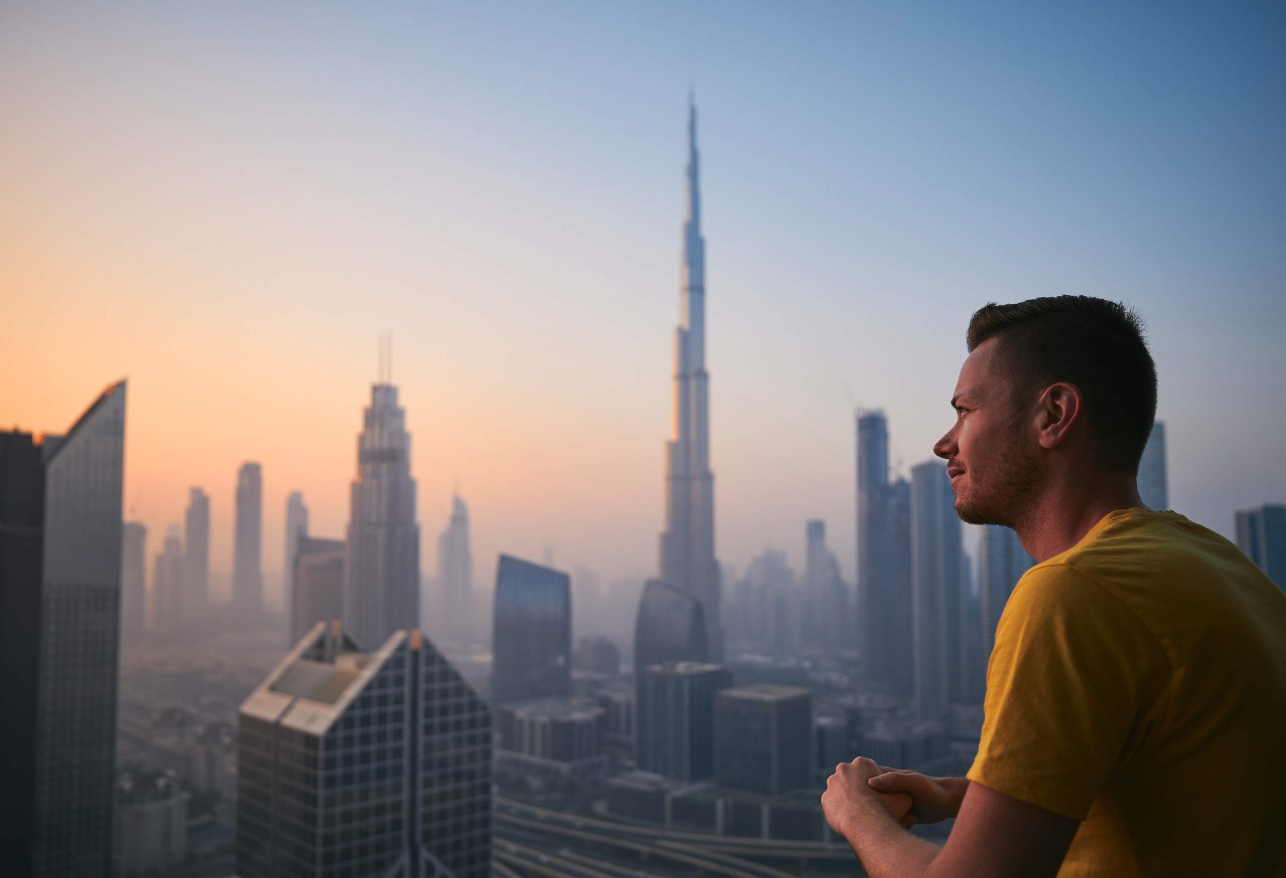 A man on a terrace looks at a city skyline with skyscrapers on a foggy morning.