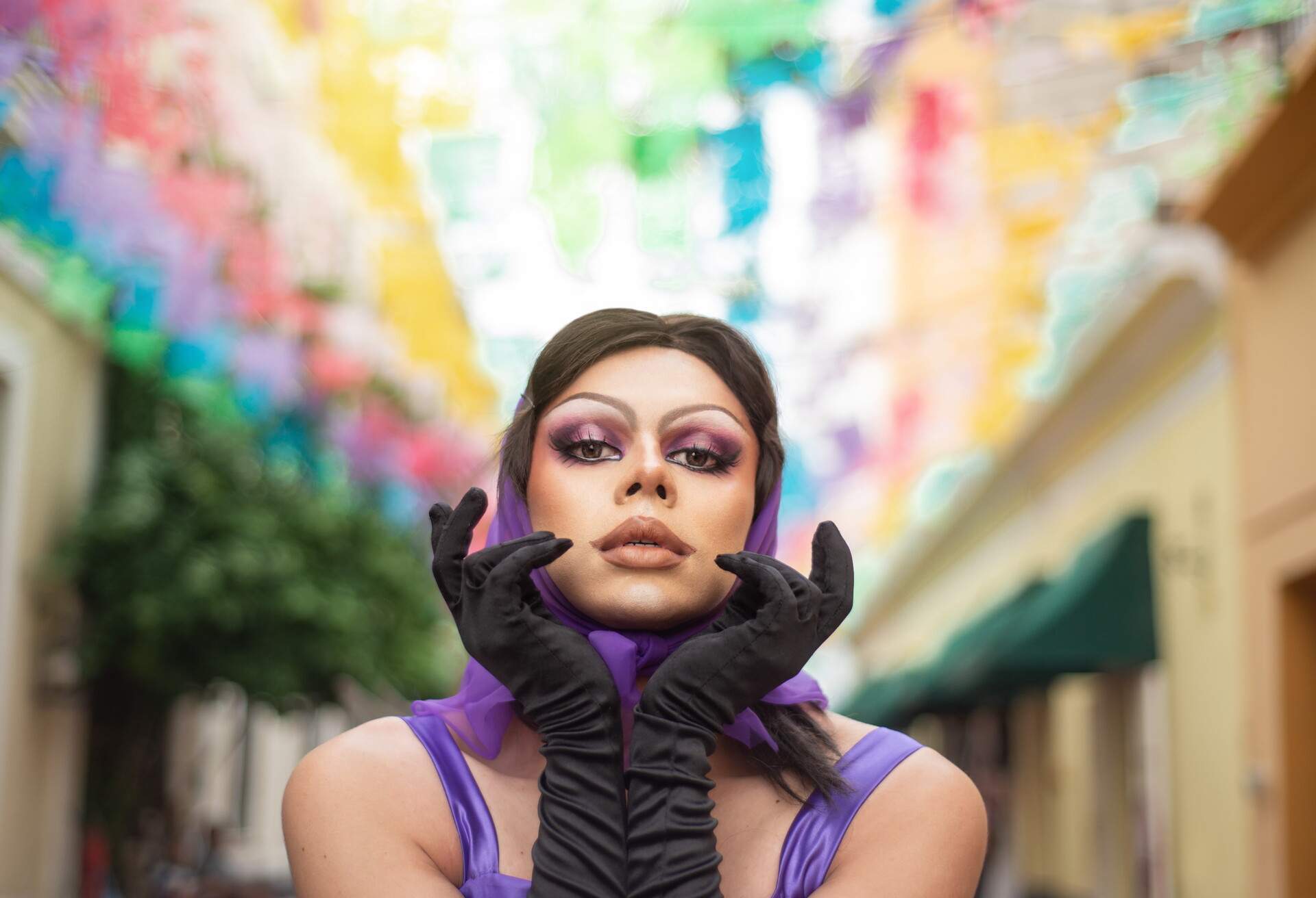 Drag Queen street portrait with multicolor background. Young man dressed as a woman looking at the camera. 