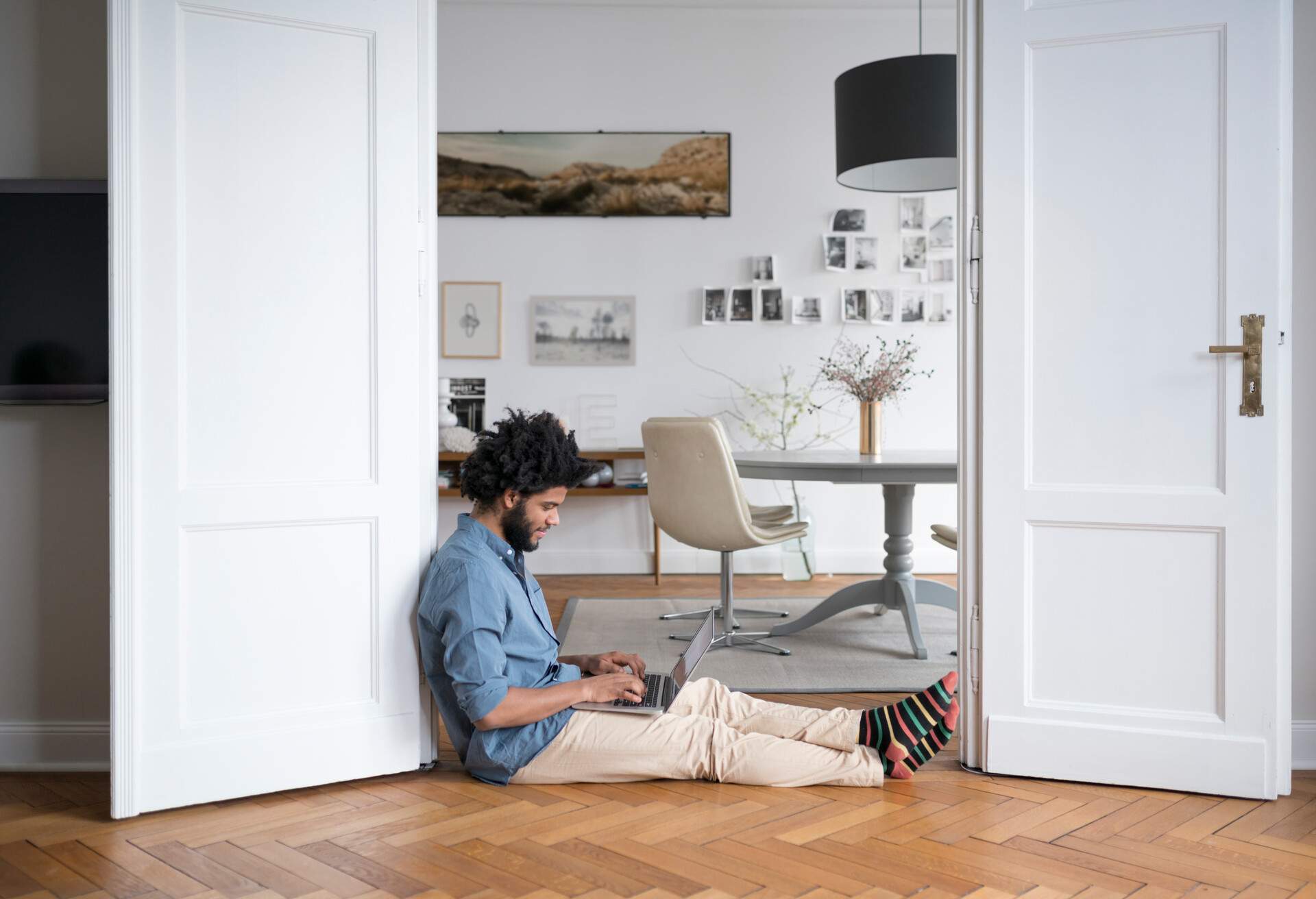 A man sits on the floor while typing on a laptop.