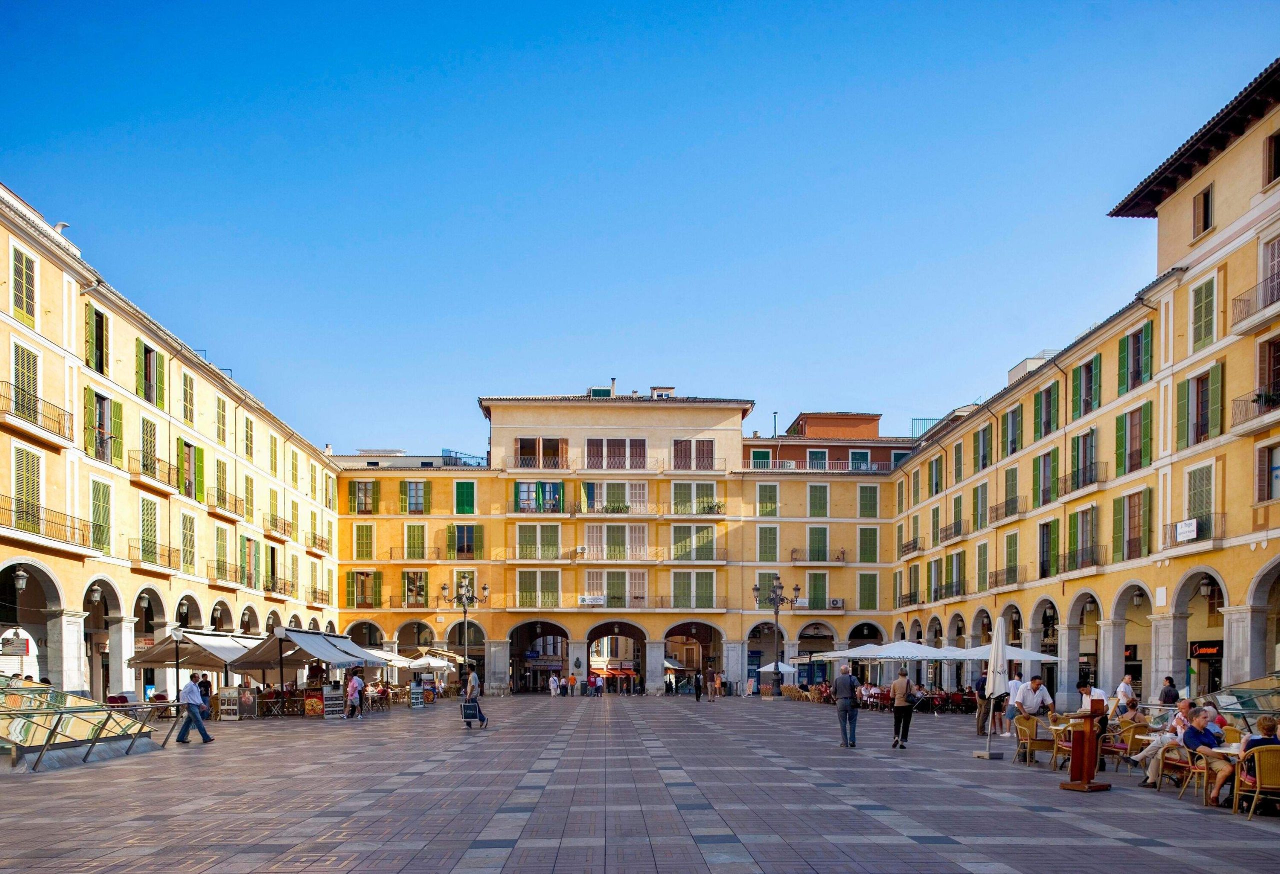 A plaza in the midst of a large building where people are wandering and eating in outdoor cafes.