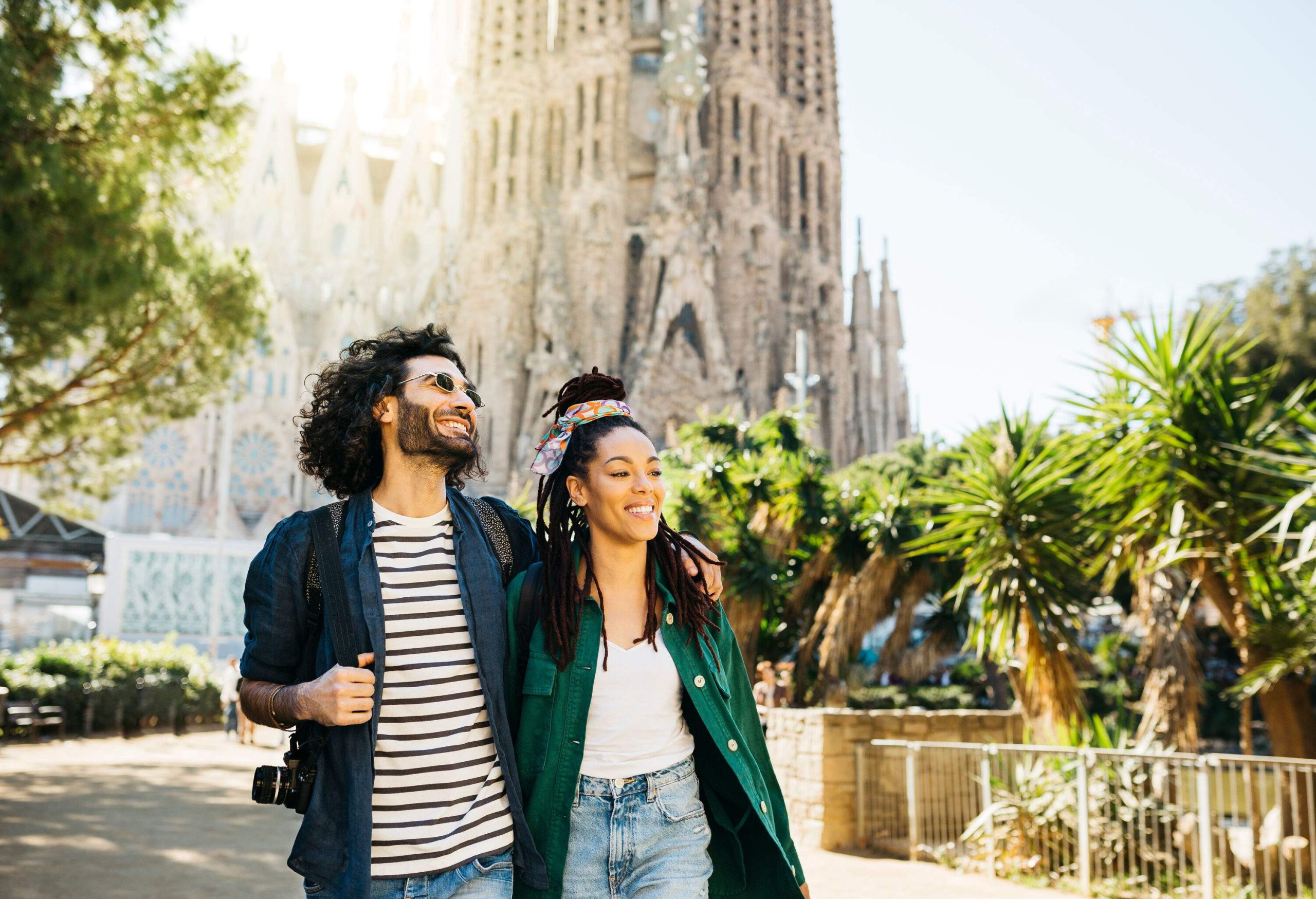 A stylish couple walking down the street with the Sagrada Familia behind them.