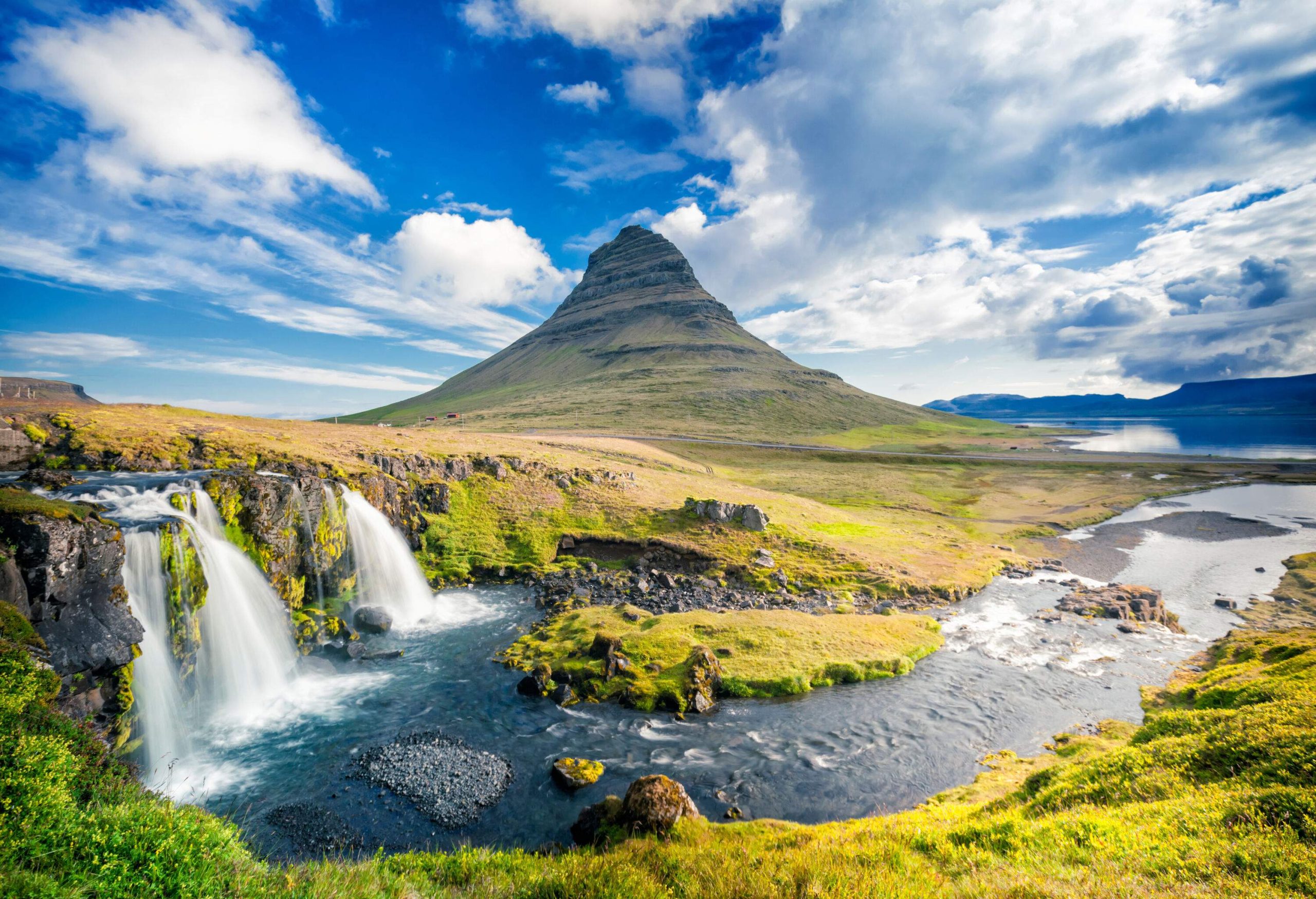 Mount Kirkjufell, a peak in the shape of an arrowhead, is surrounded by a beautiful green environment and a waterfall that runs into the river.