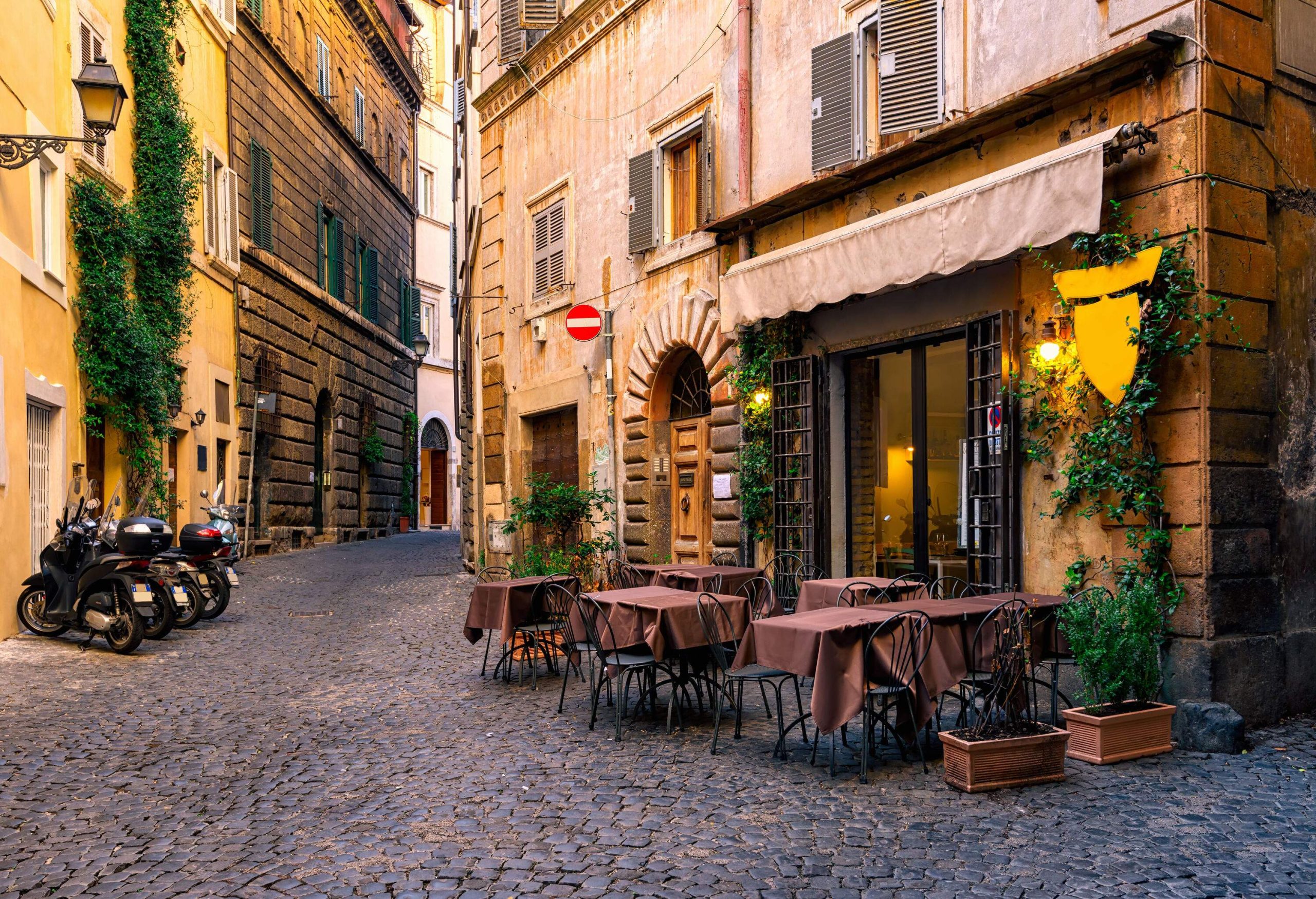 A cosy ambiance of an old stone-paved street, rustic buildings, and charming al fresco dining areas.