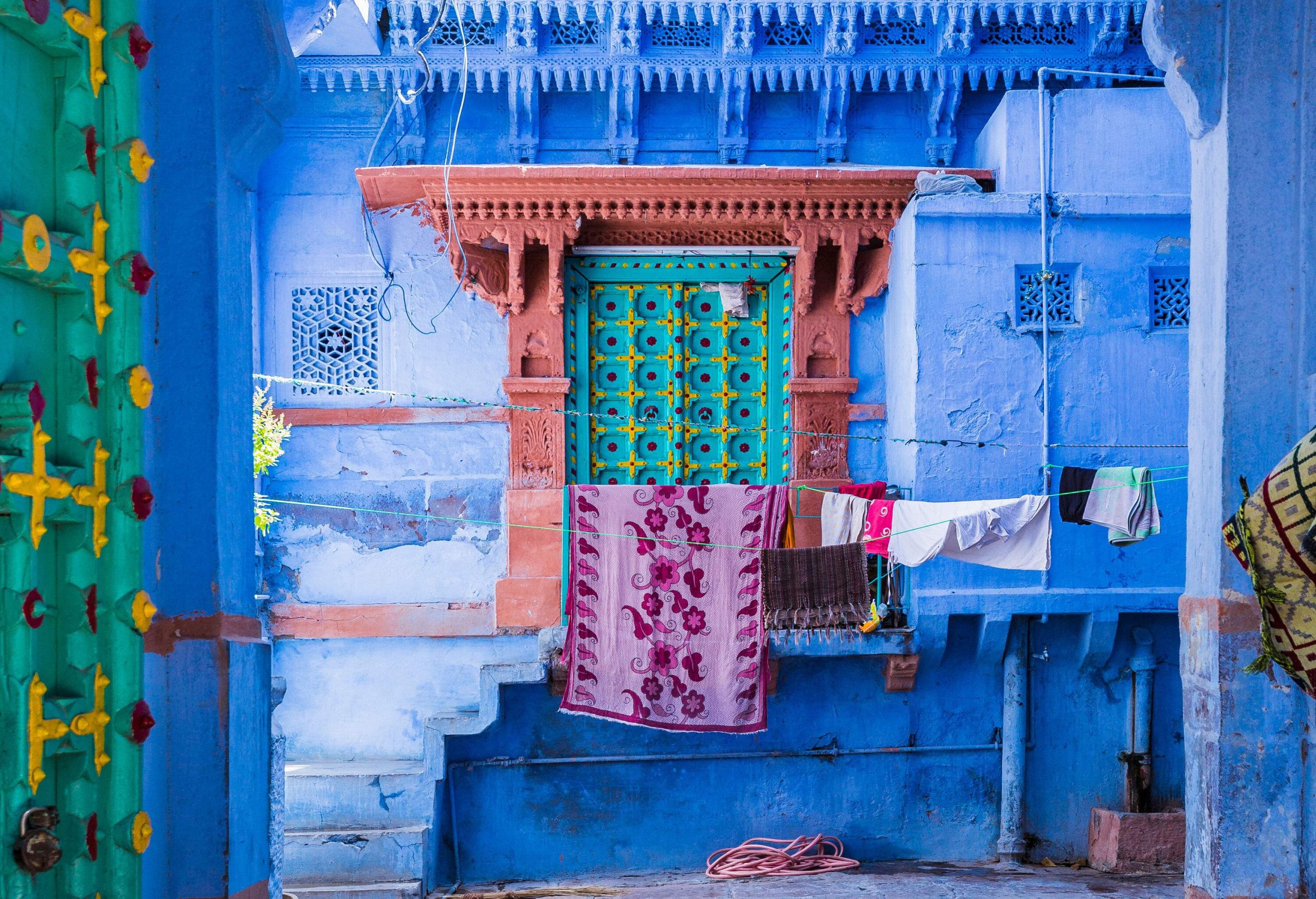 An archway frames a blue building with a decorated window beside the hanging laundries.