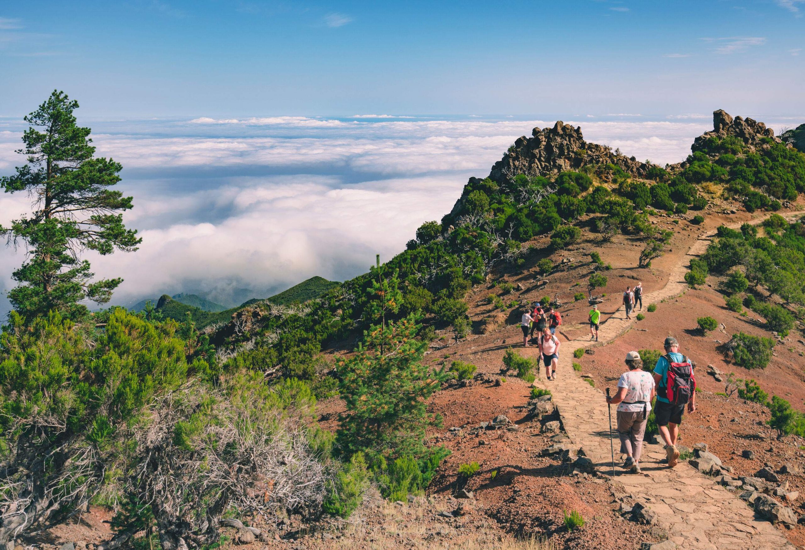 People walking on a stone pathway on a mountain with overlooking views of the horizon covered in clouds.