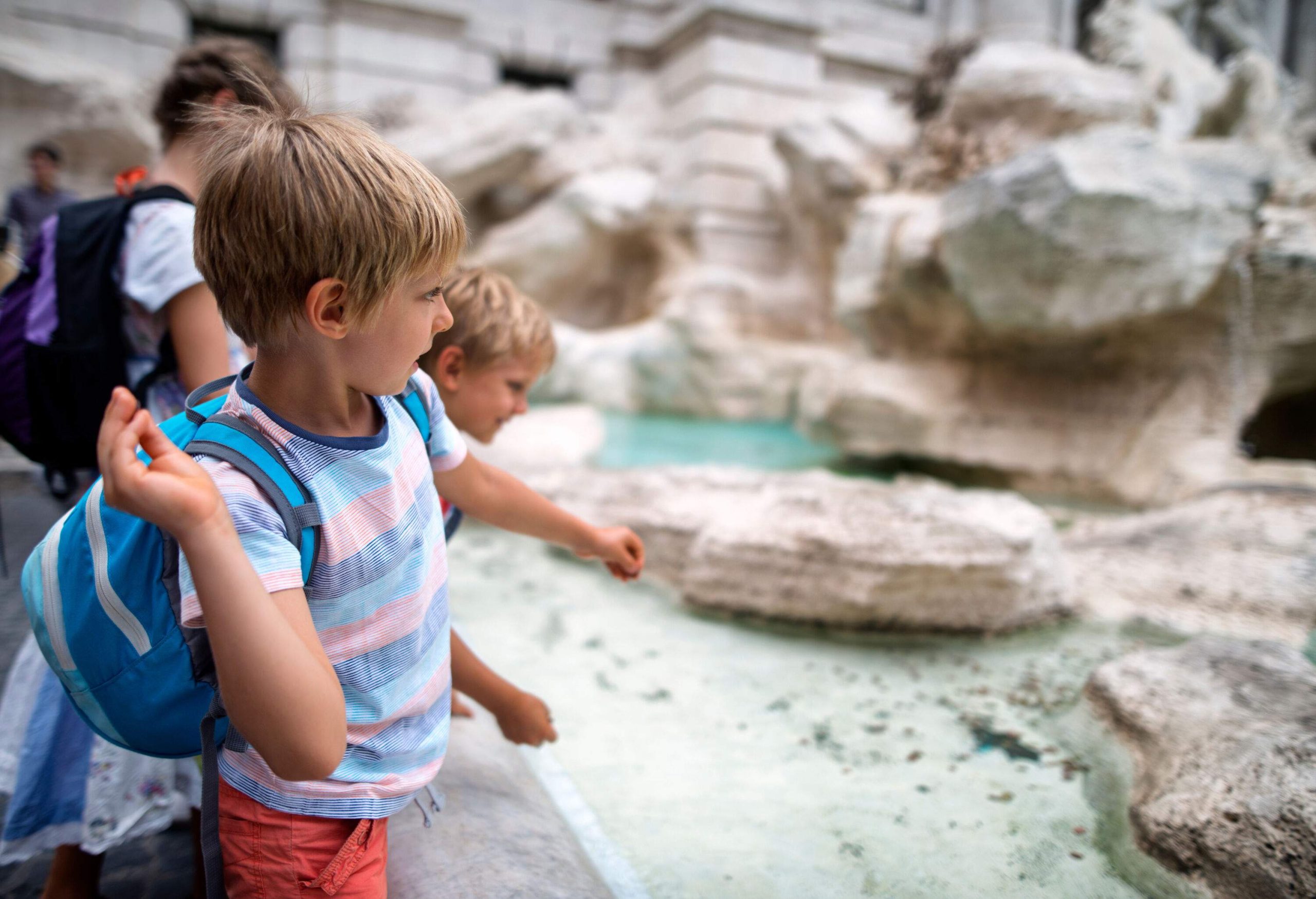 Excited kids throw coins onto the sparkling waters of the pond at the base of the Trevi Fountain.