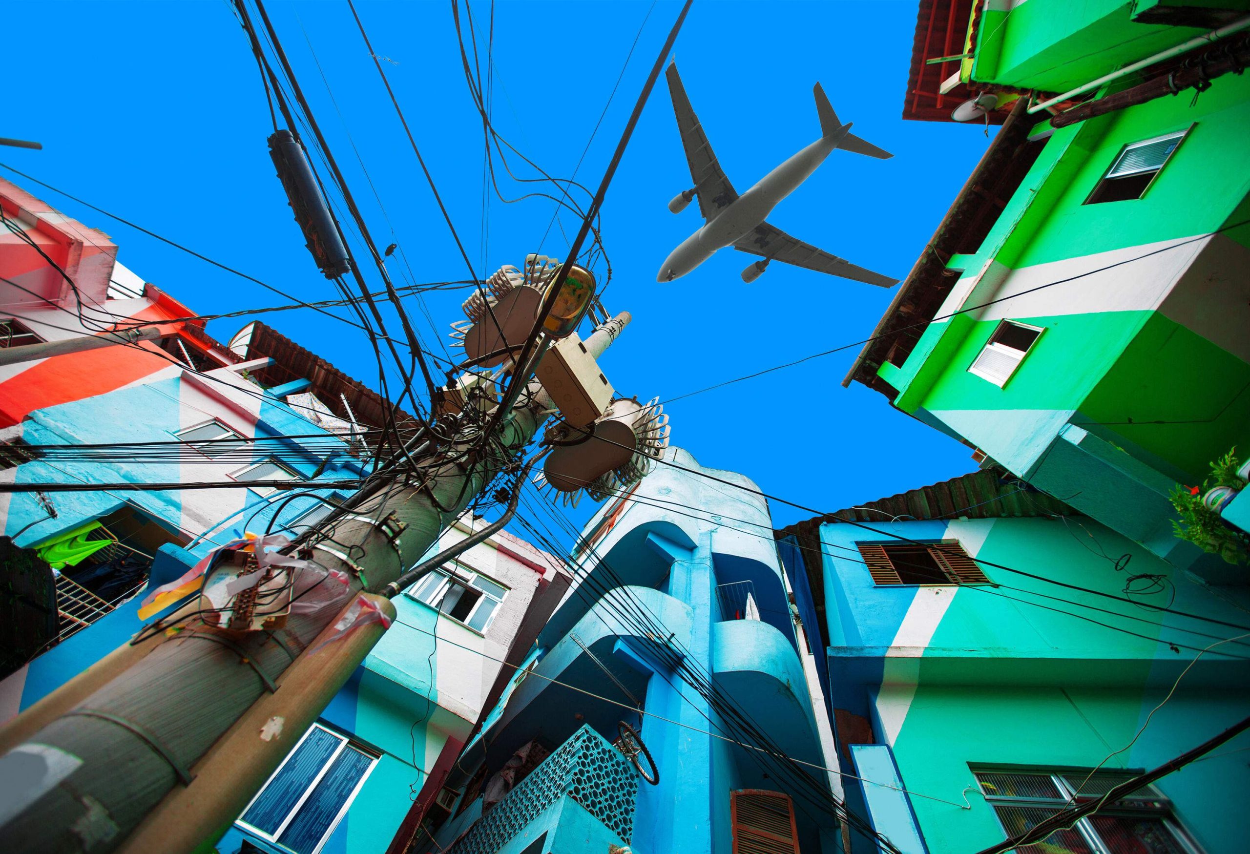 An airplane flying across the blue sky over the gap between colourful buildings.