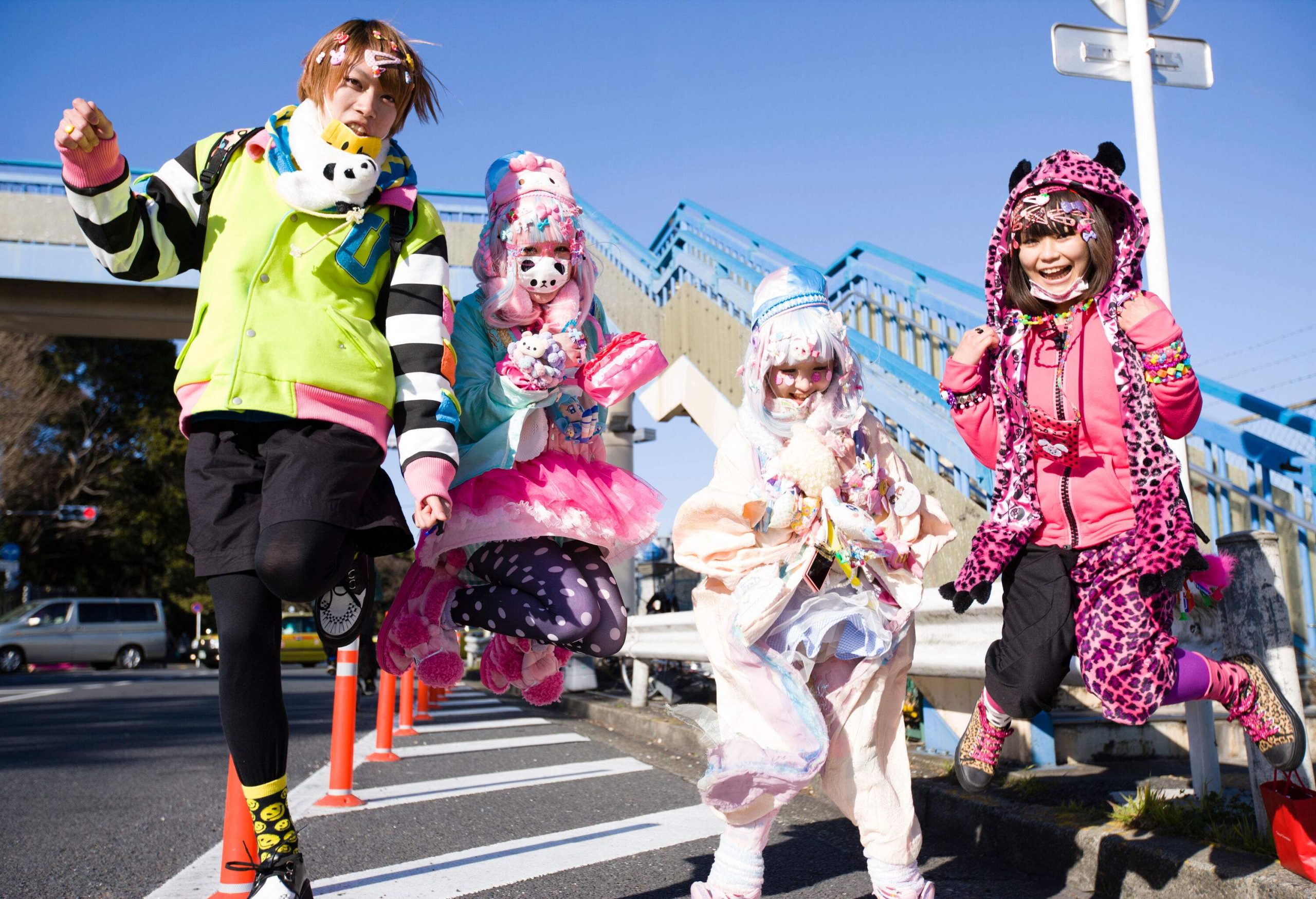 Four joyful individuals wearing vibrant clothing were captured mid-air while doing a jump shot in a street.