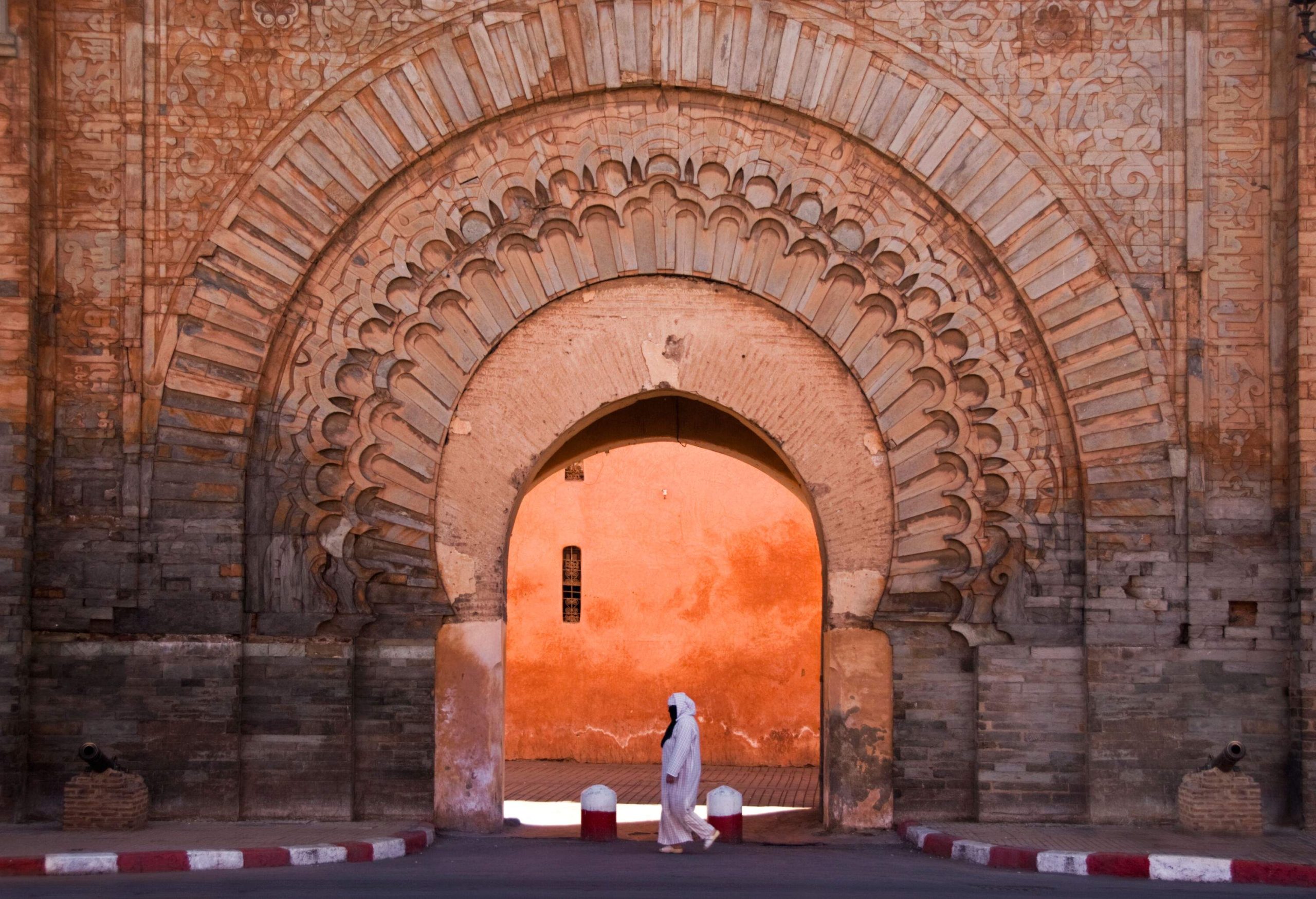 An individual in traditional white Arab clothing passing by an ornated arched gate.