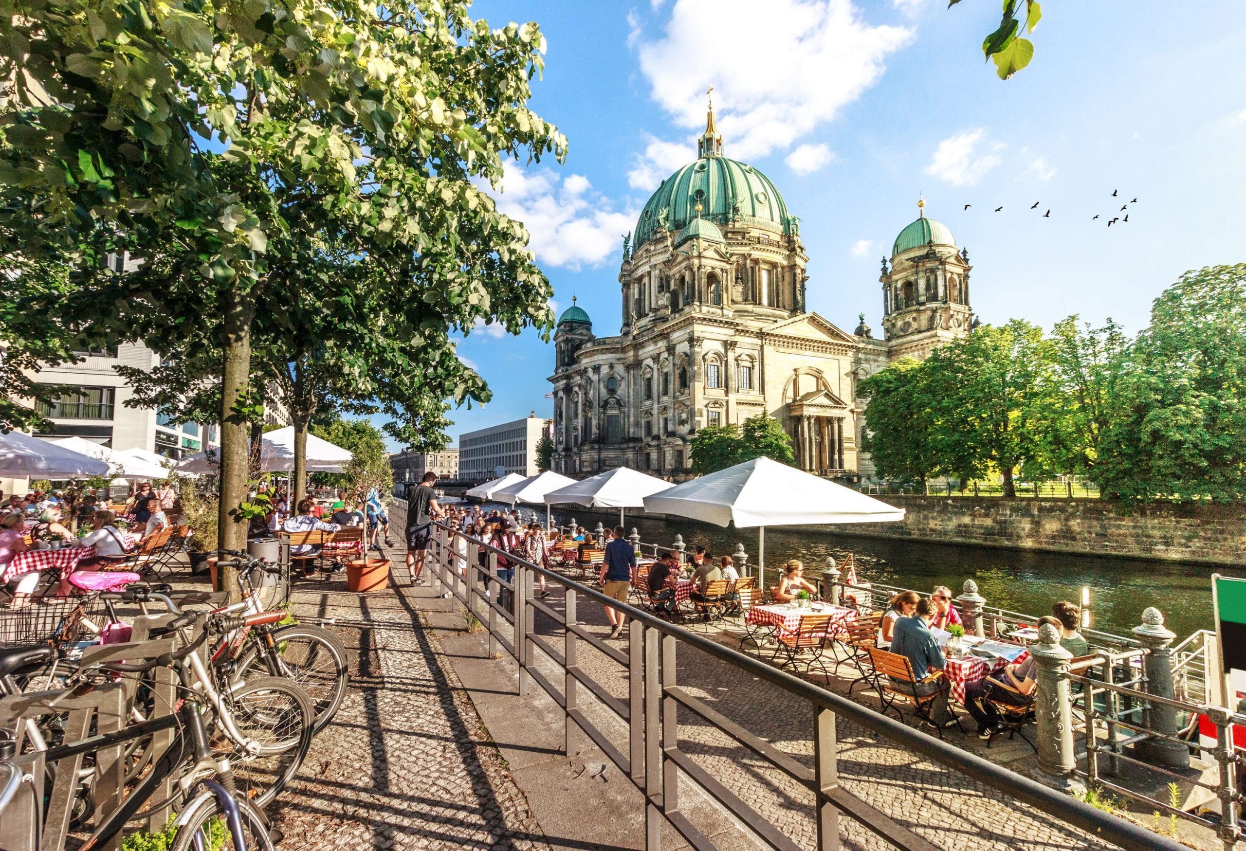 An outdoor café by the river with the Berlin Cathedral in the background.