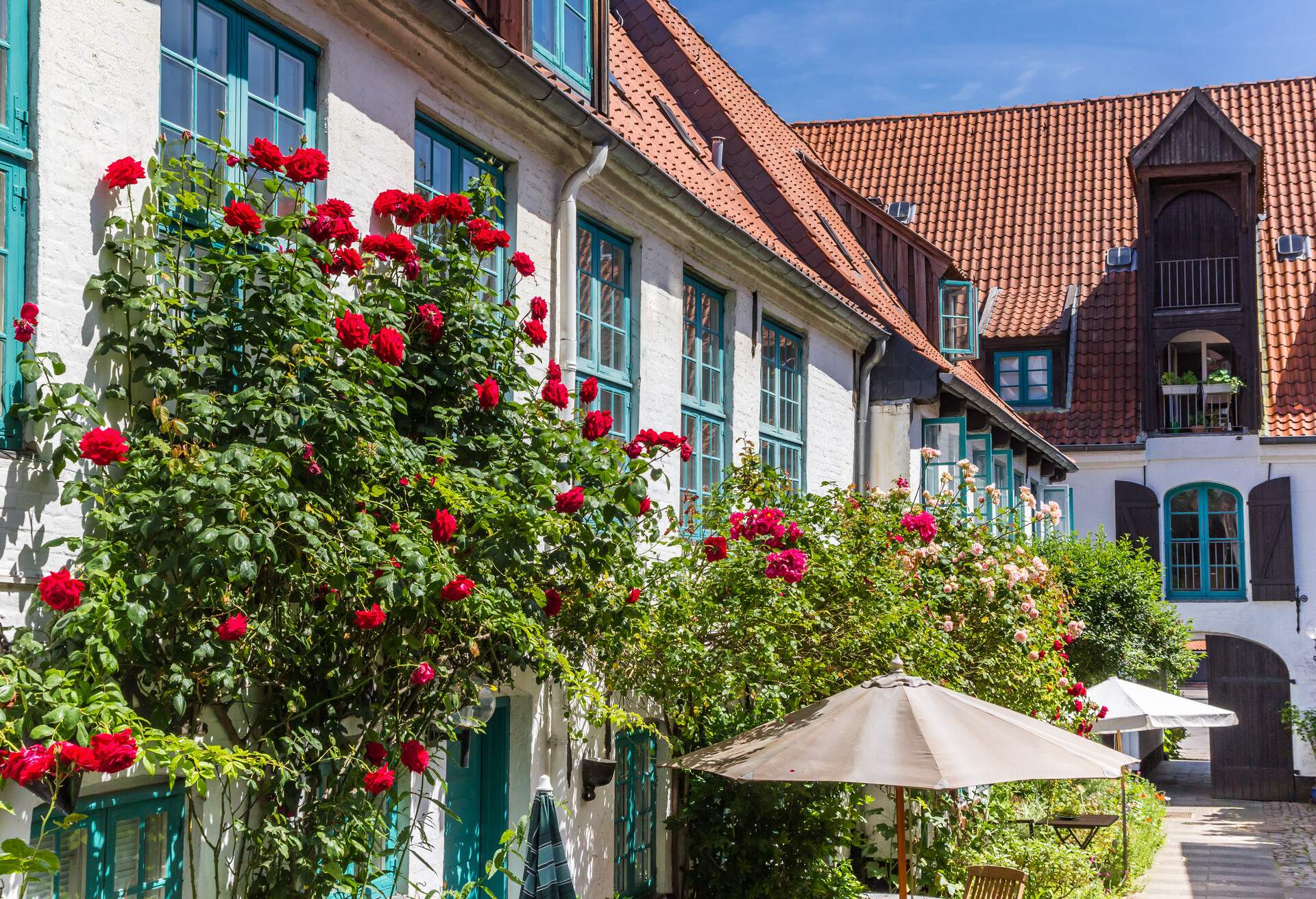 A white house with a red brick roof adorned with colourful flowering plants.