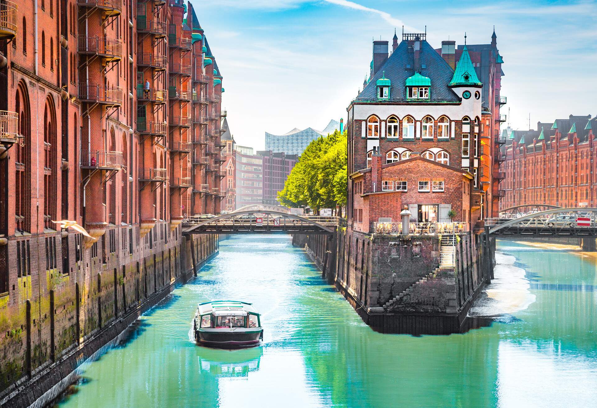 A boat sails on a canal alongside a famous historic building in a large warehouse district.