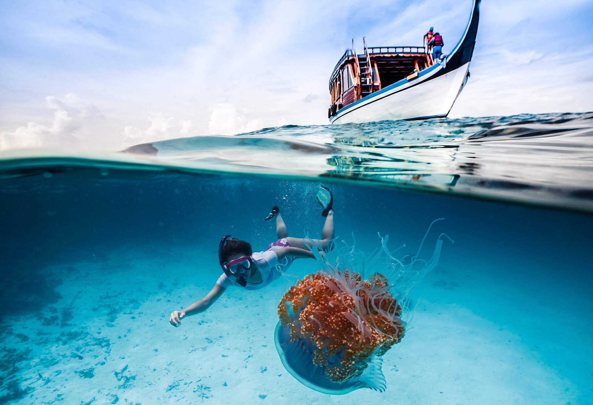 A snorkeller catches a glimpse of a beautiful jellyfish underwater, above a boat.
