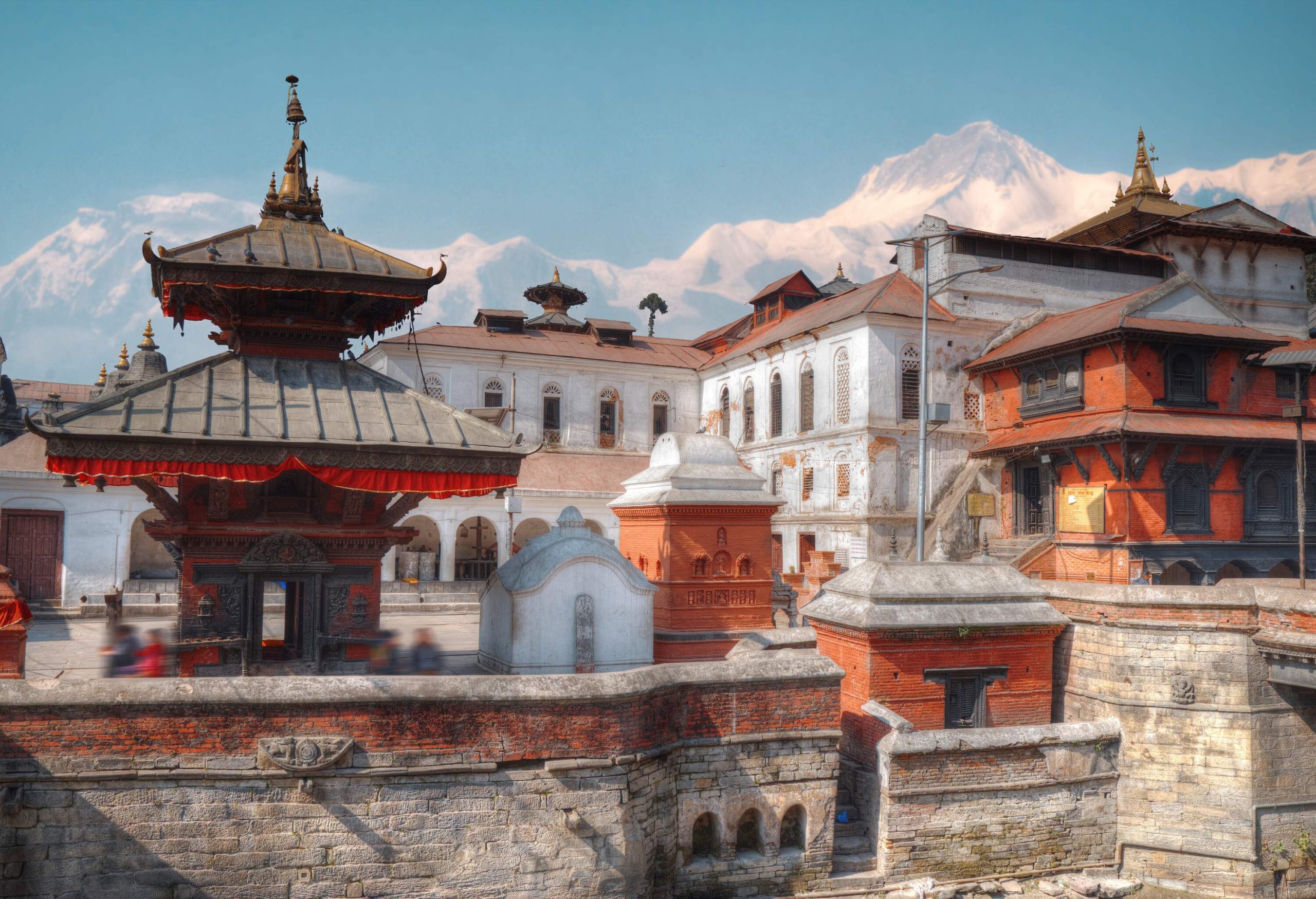 Temple complexes enclosed in stone walls, with a snow-covered mountain range in the background.