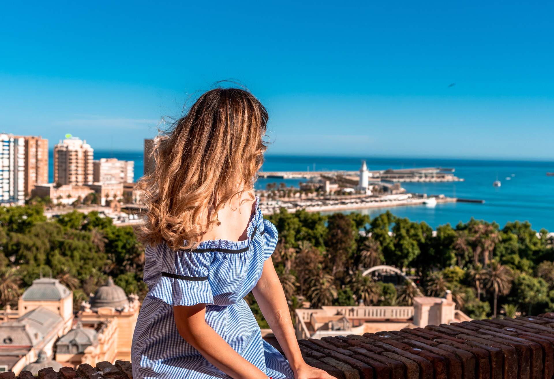 A woman in a blue dress looks at classic seaside cityscape from a vantage point.