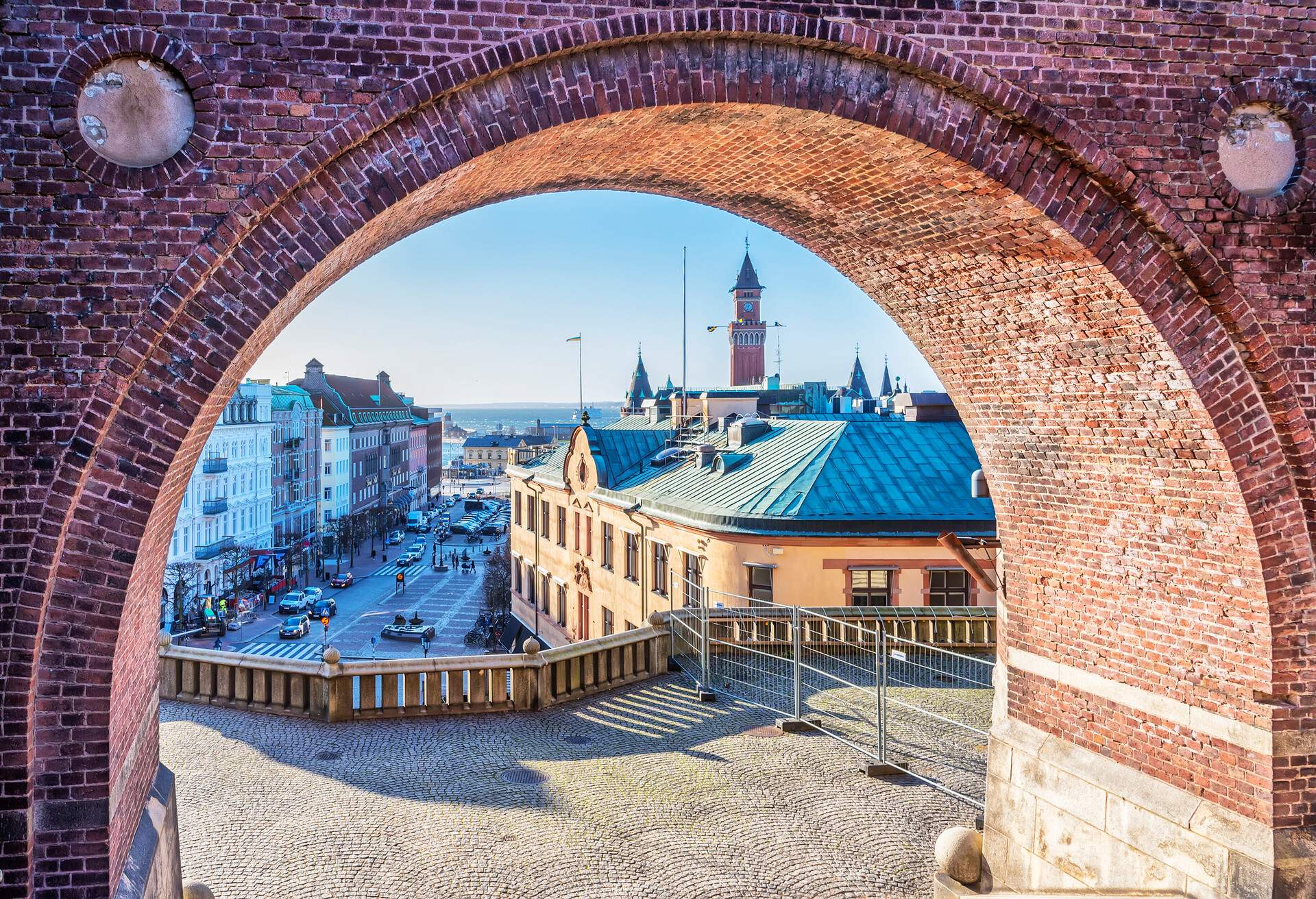 A brick archway leading to a terrace overlooking a bustling city street.