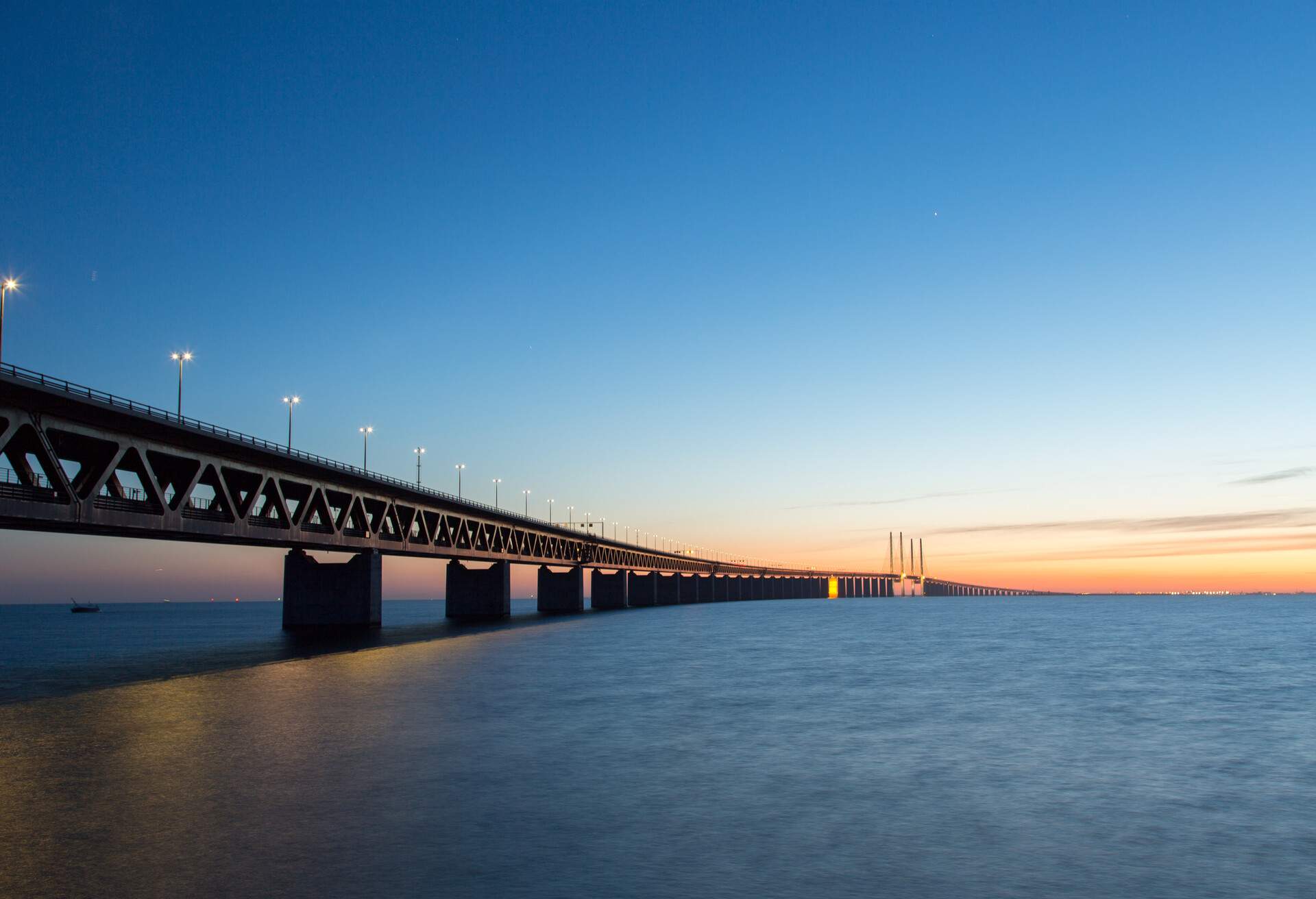 A large body of water with a long bridge lit by lampposts.