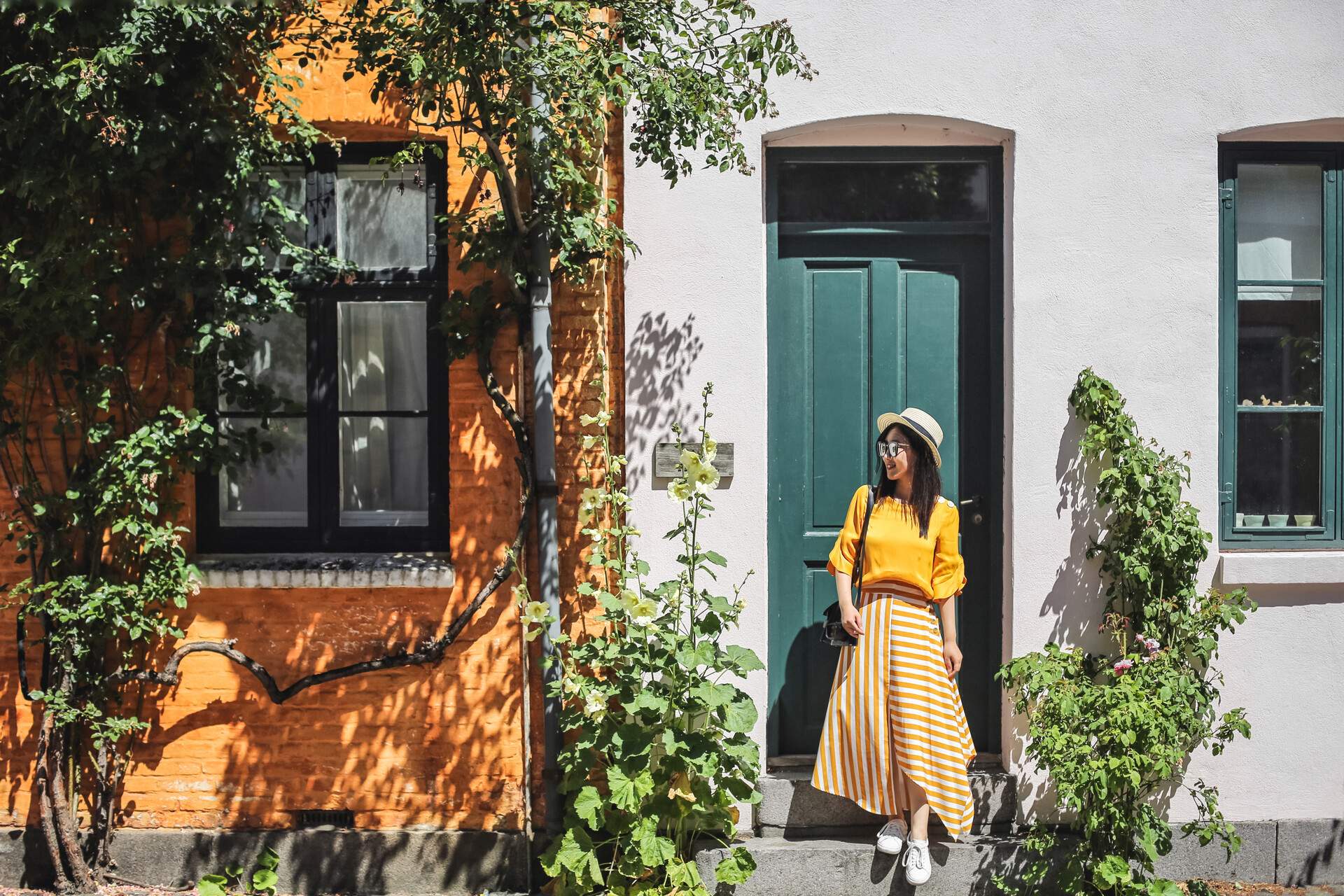 A smiling young lady steps down in front of a green door on a sunny day.