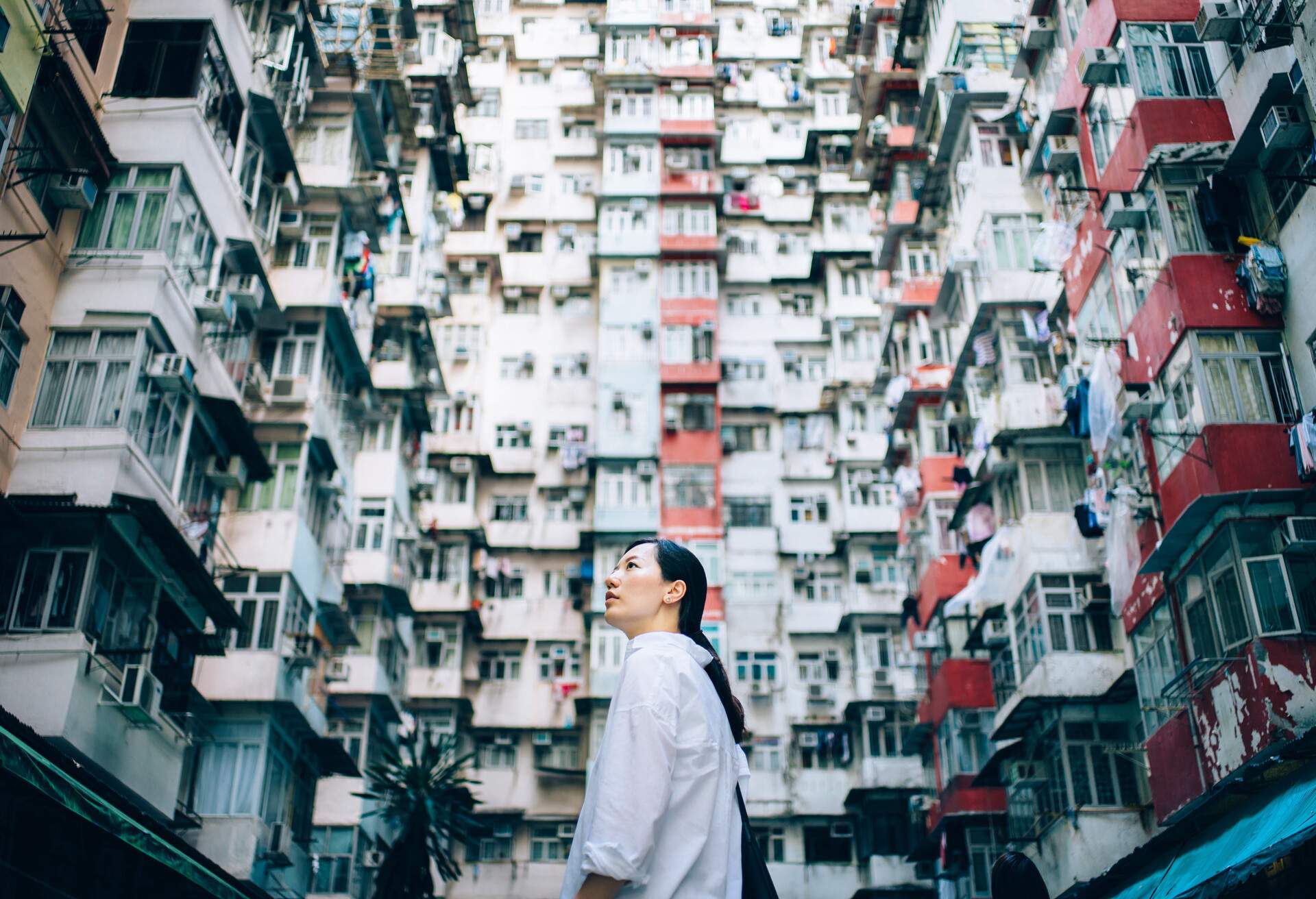 A captivating low-angle view of a woman standing amidst a charming backdrop of old traditional residential buildings, gazing up with wonder and admiration.