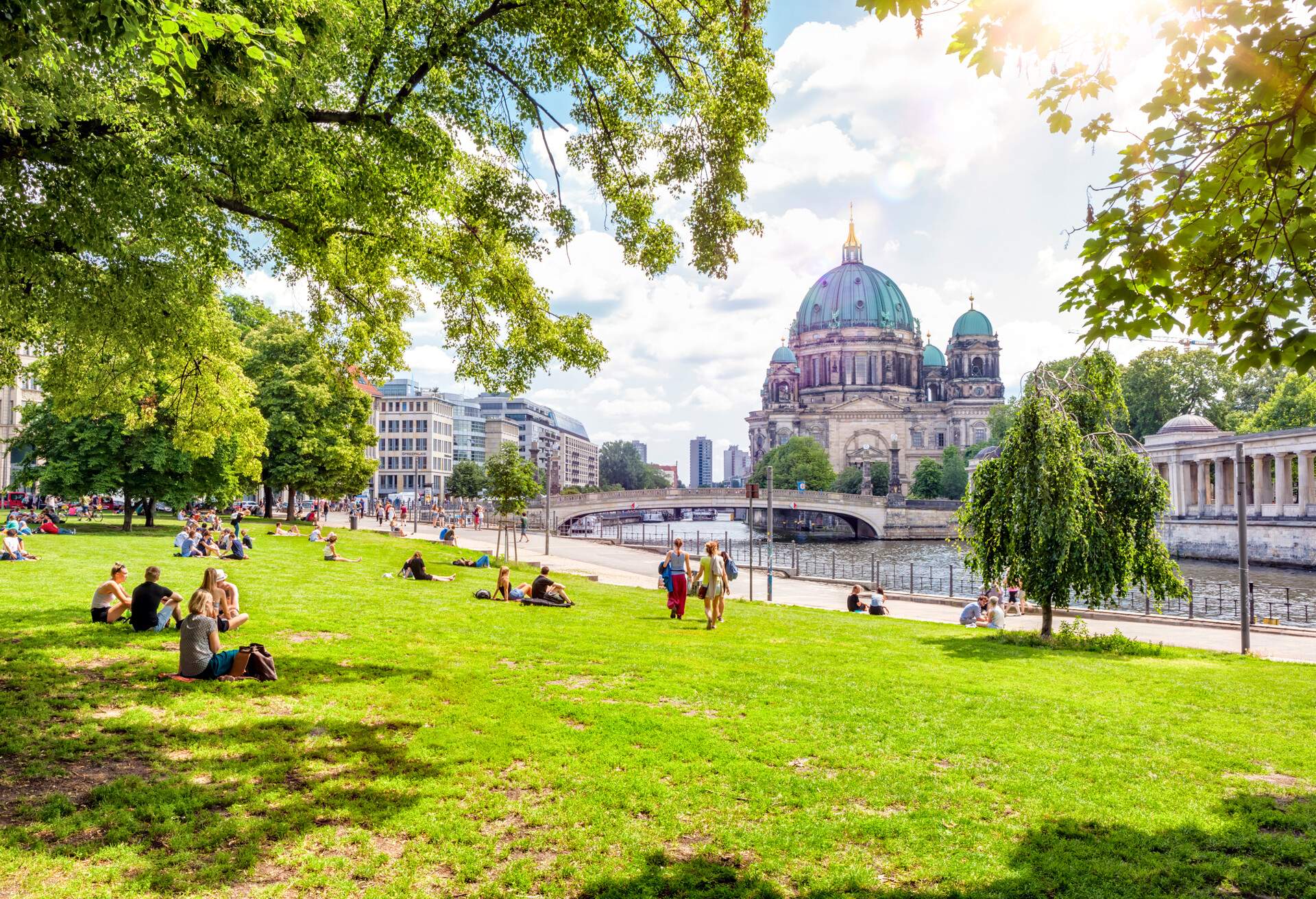 People enjoying a sunny day at a park by the river overlooking the Berlin Cathedral.