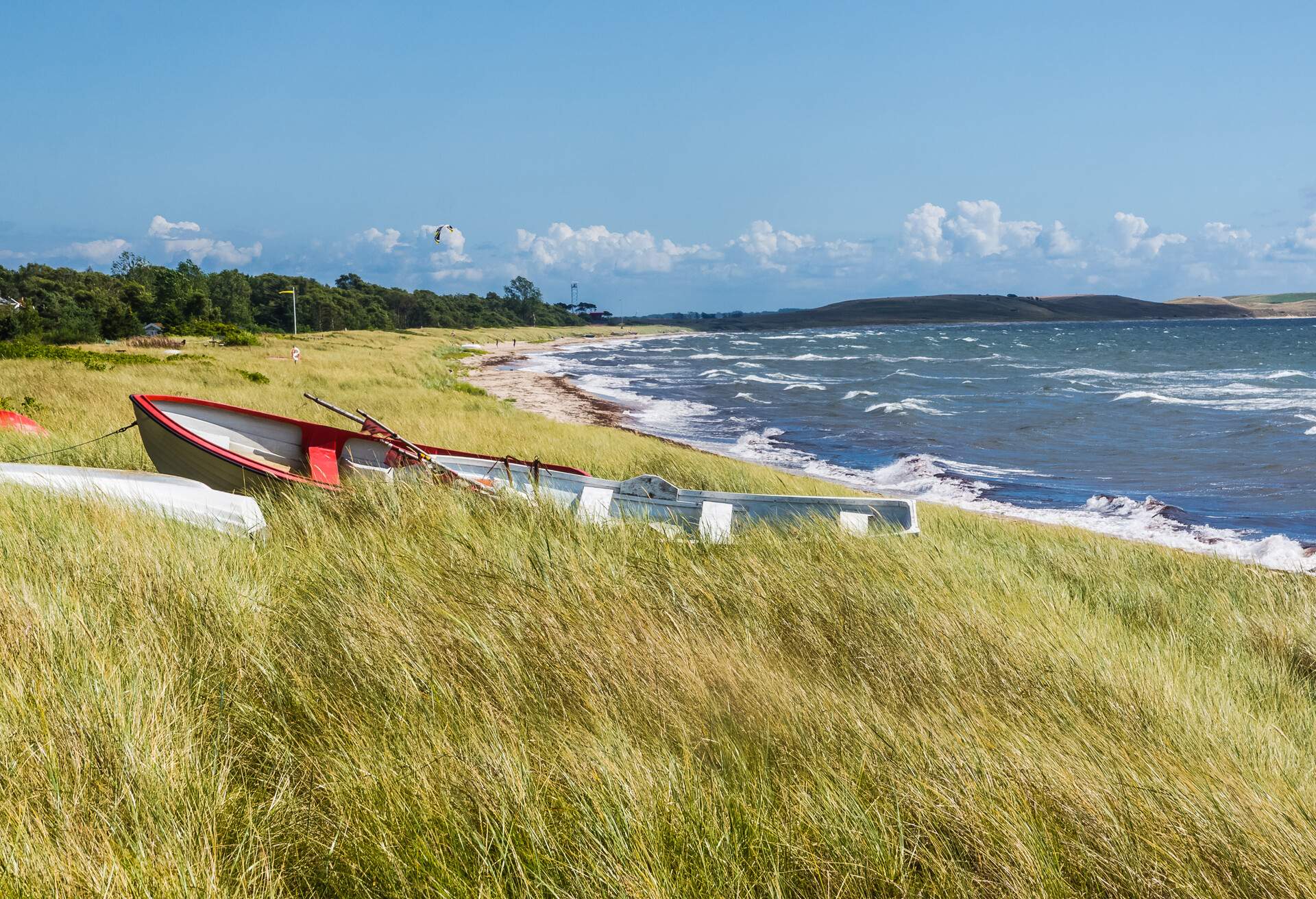 A red and white boat left on the bush alongside a wavy shore on a clear sunny sky.