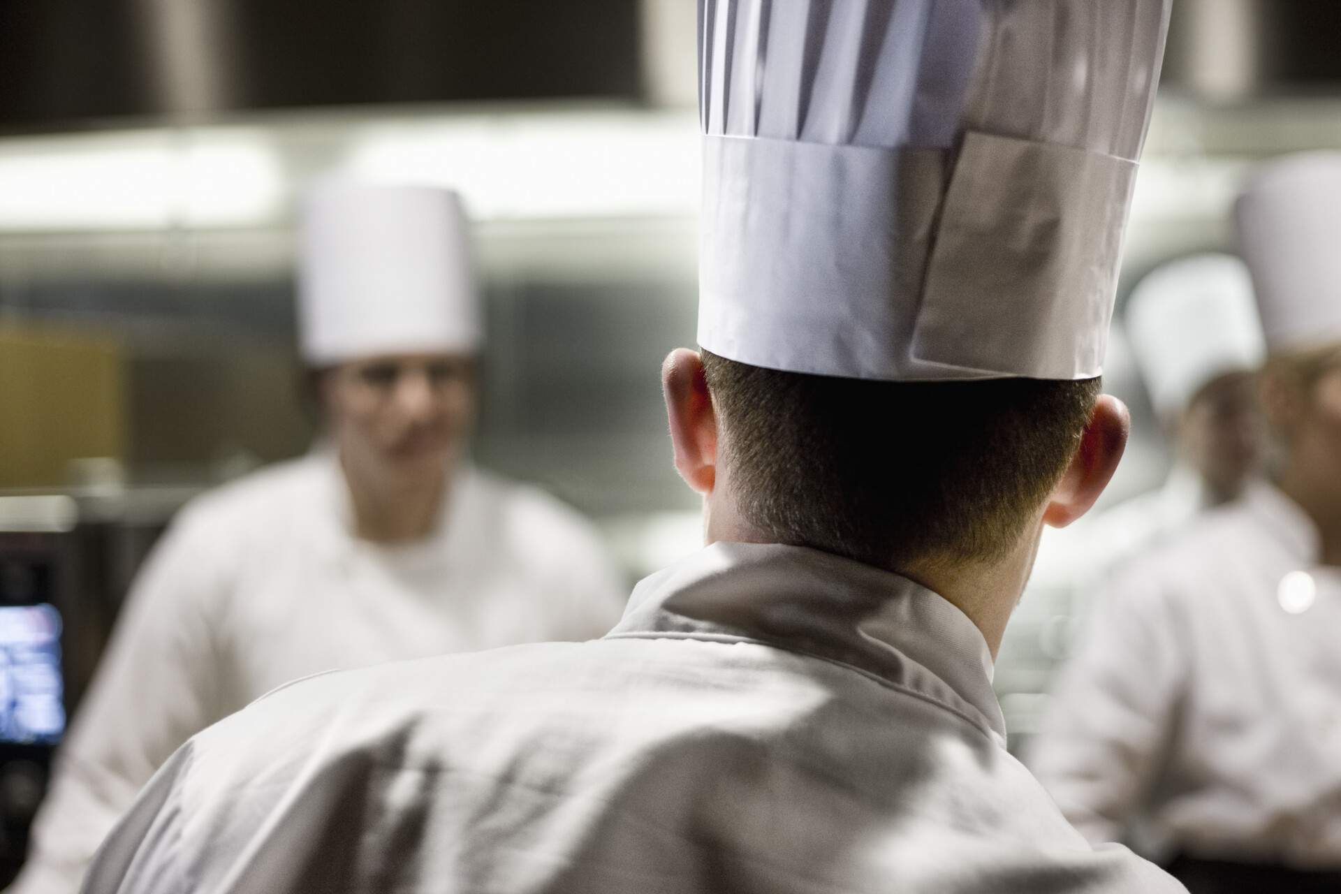 Group of chefs wearing toque hats inside a kitchen.