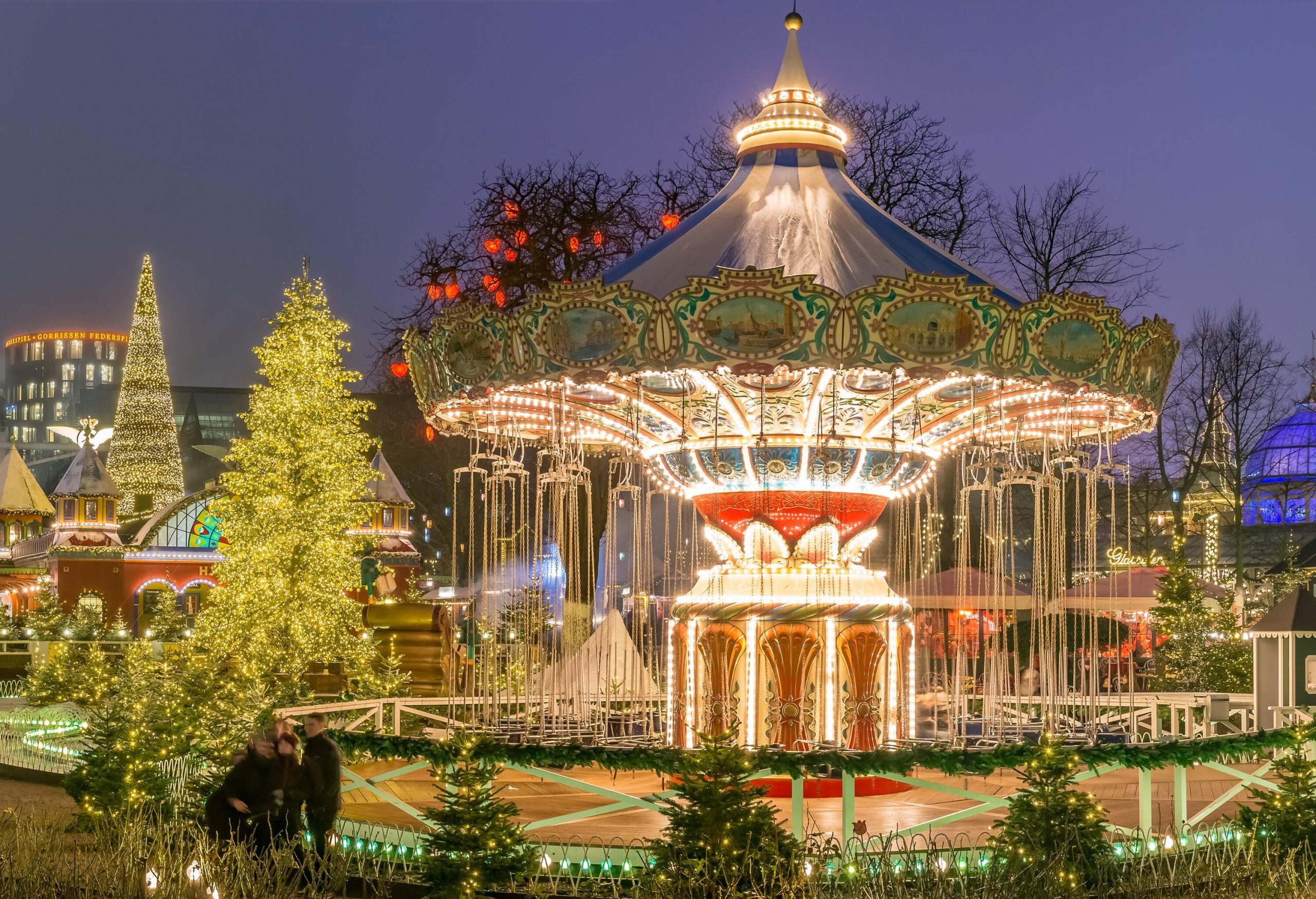 Magical light displays at an amusement park featuring a carousel and surrounding trees illuminated at night.