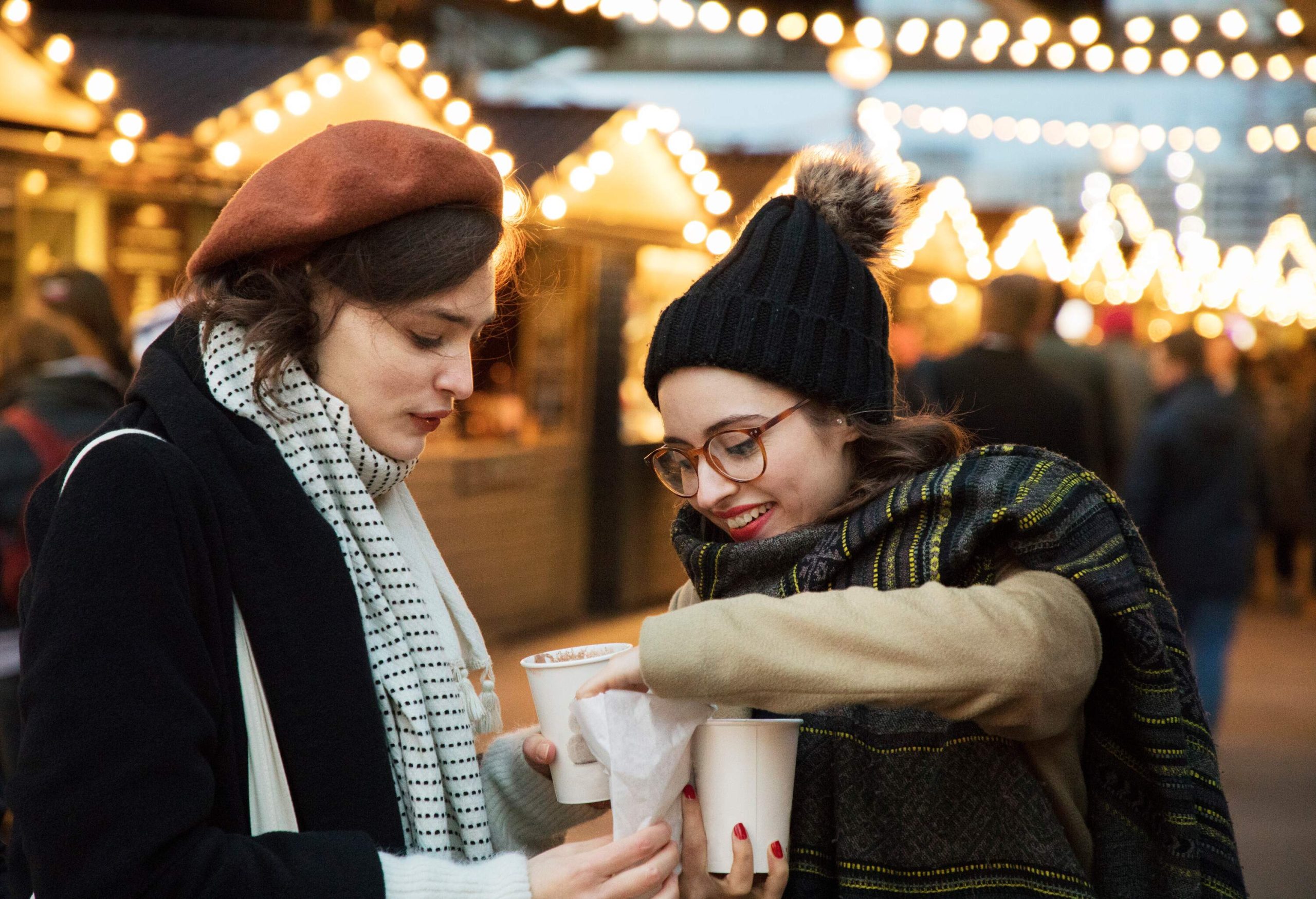 Two female friends sharing food and drinks at Christmas market