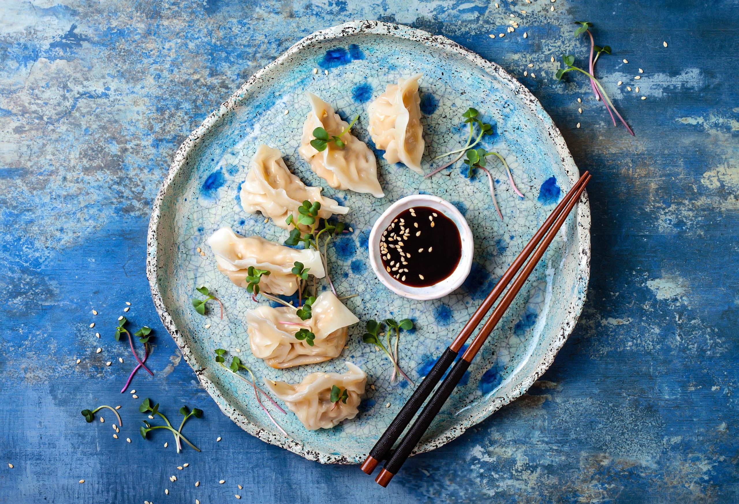 Chinese dumplings served with sesame seeds soy sauce and chopsticks.