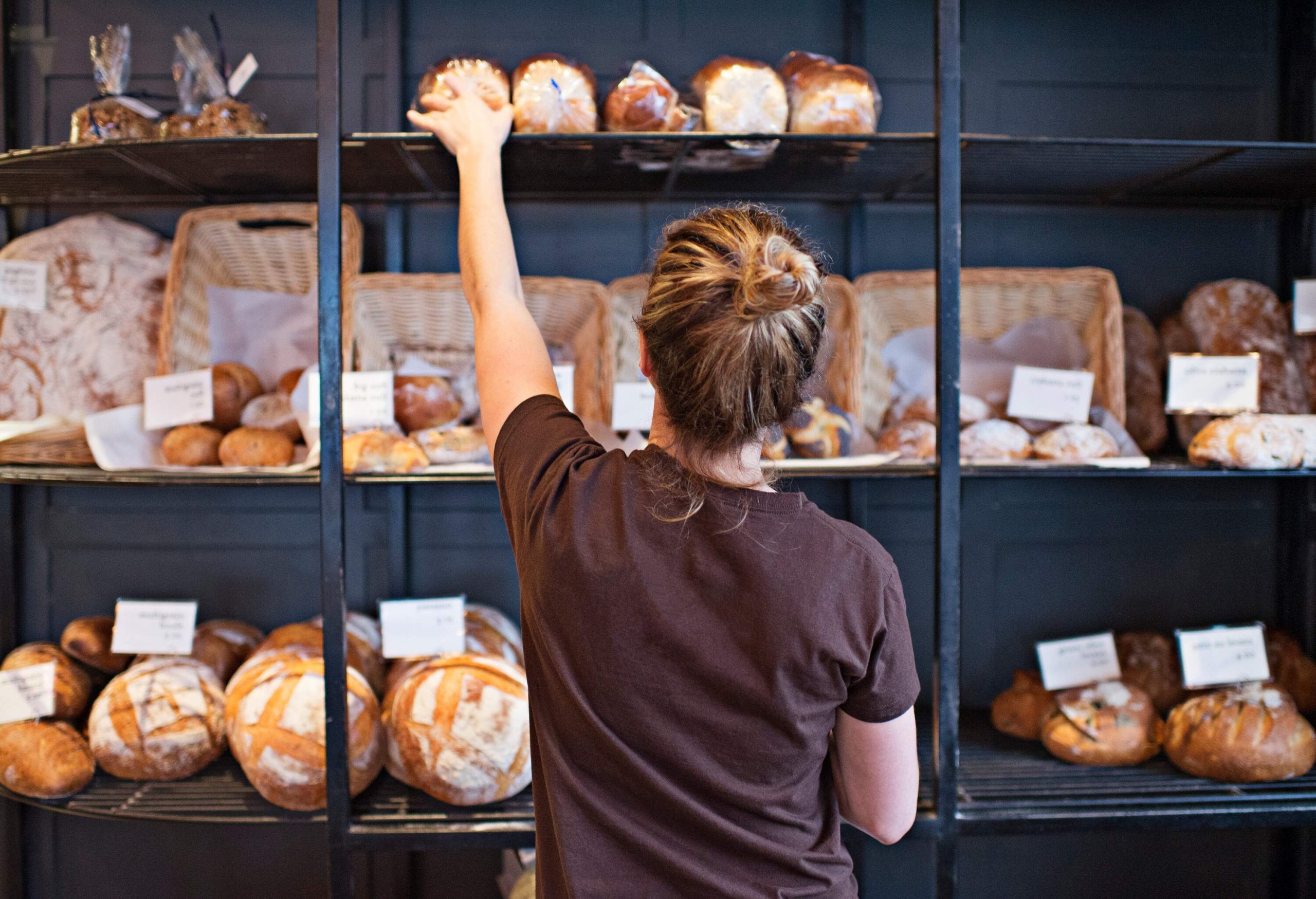 A woman fills up the shelves with baked loaves of bread.
