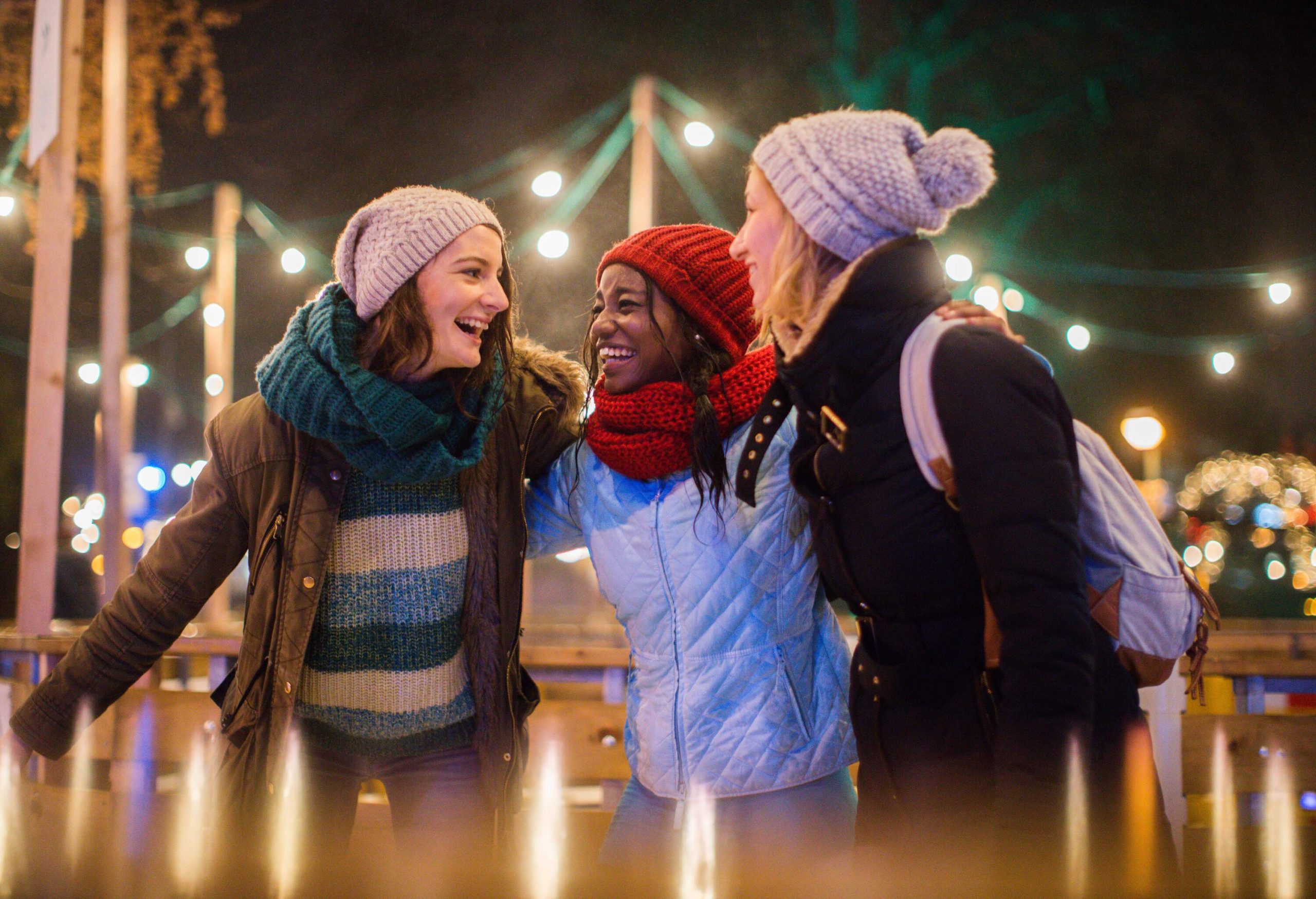 Three people wearing winter clothes having fun in the Christmas market.