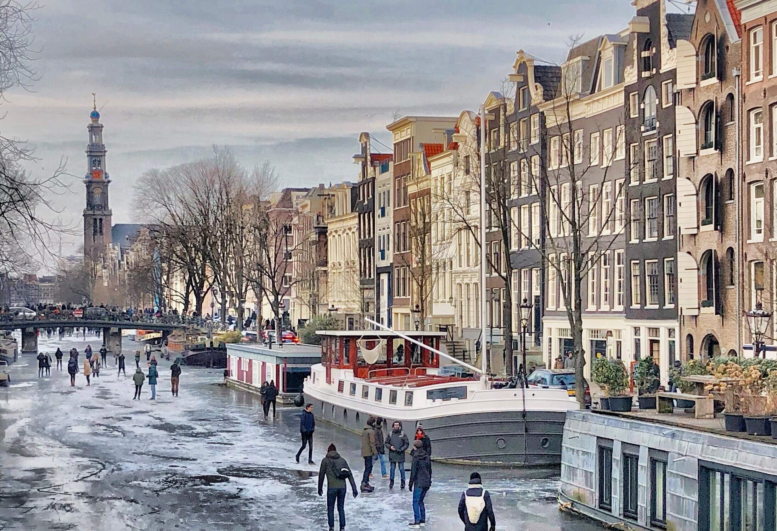 People skating on a frozen canal along the houseboats and adjacent city buildings.