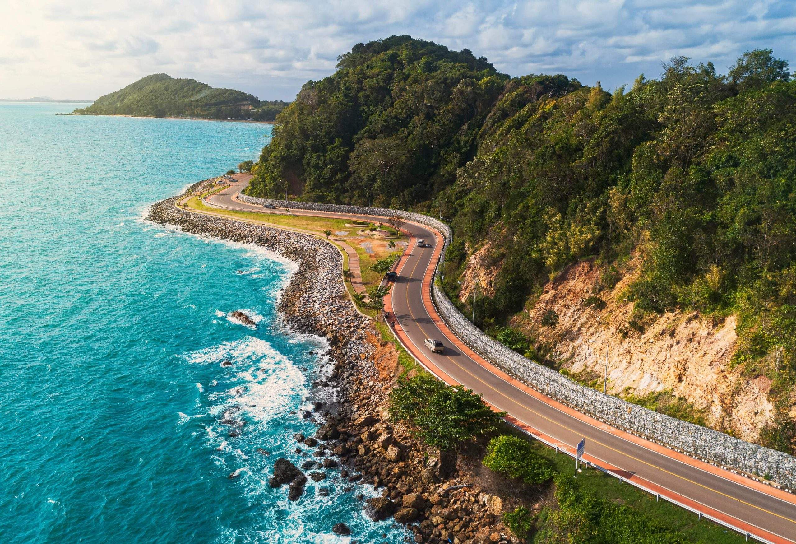 Cars travelling on a coastal road along the forested cliffs with vast ocean views.